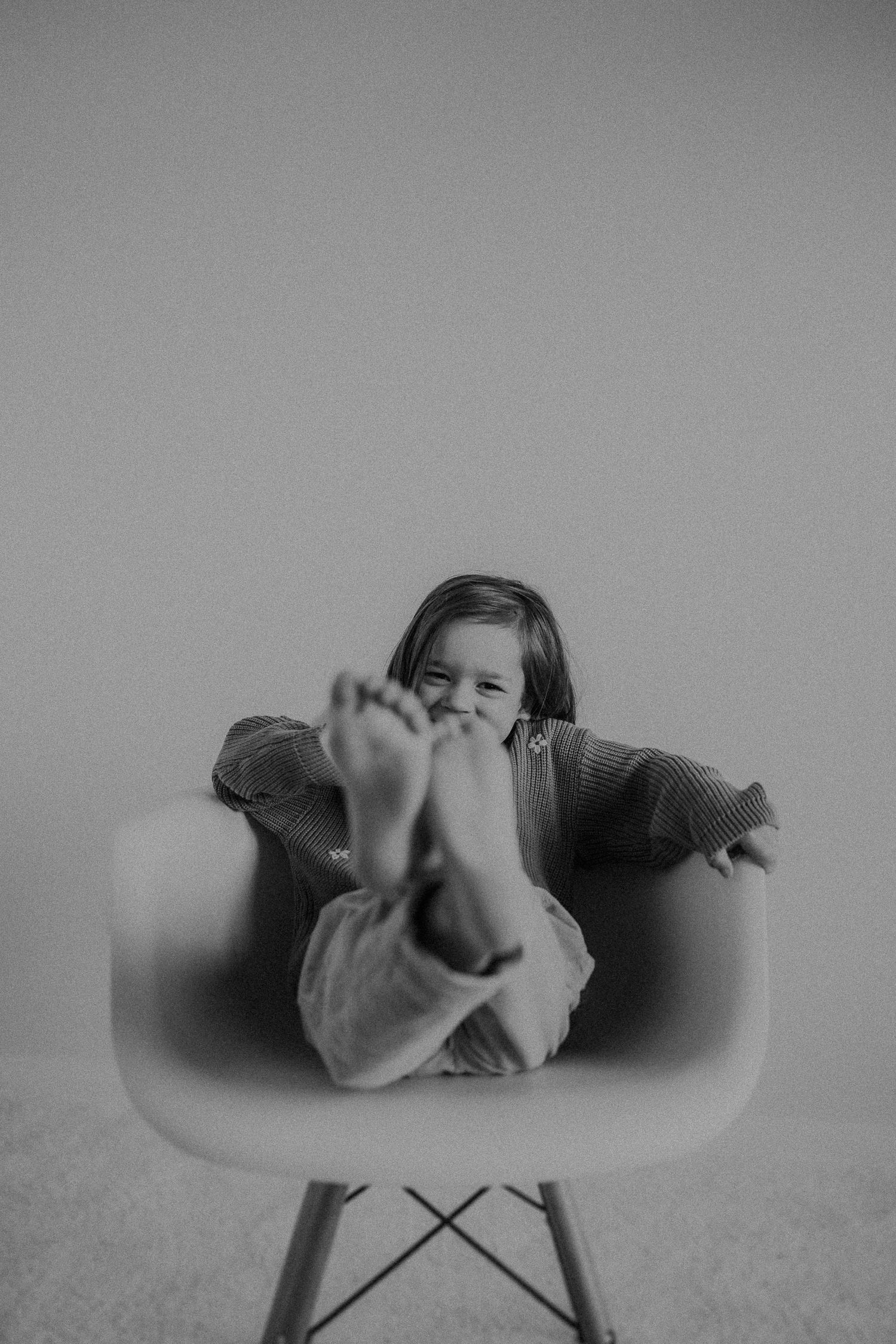 Playful black and white portrait of child lounging in modern chair with feet up.