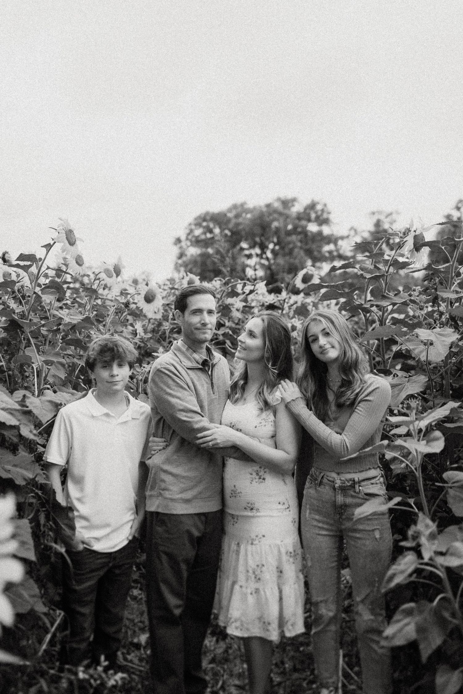 A black and white portrait of a group standing among tall sunflowers.