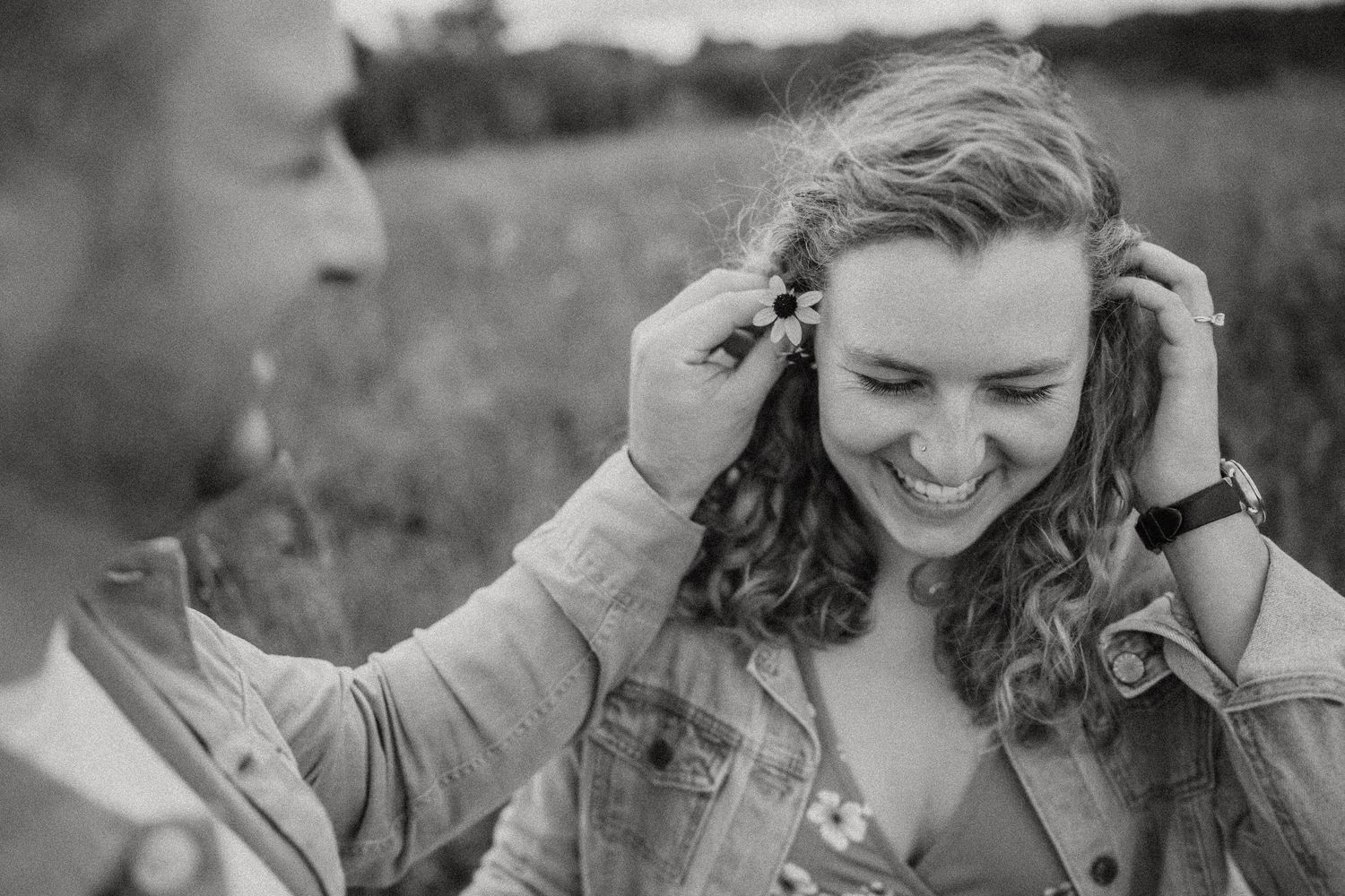 An intimate black and white portrait of a couple sharing a playful laughing moment outdoors.