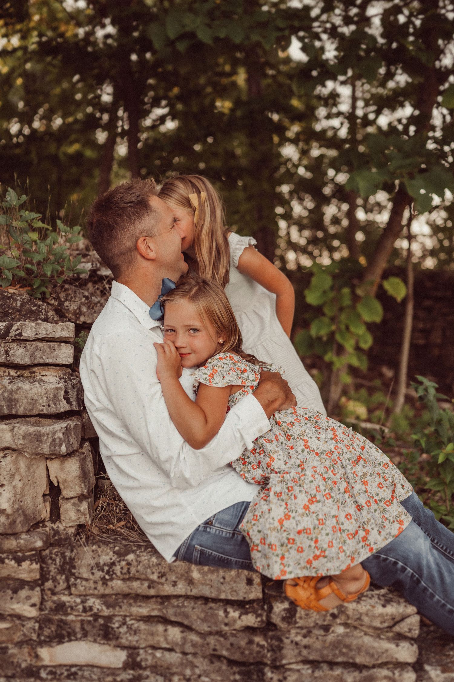 Intimate family portrait on stone steps surrounded by green foliage at sunset.