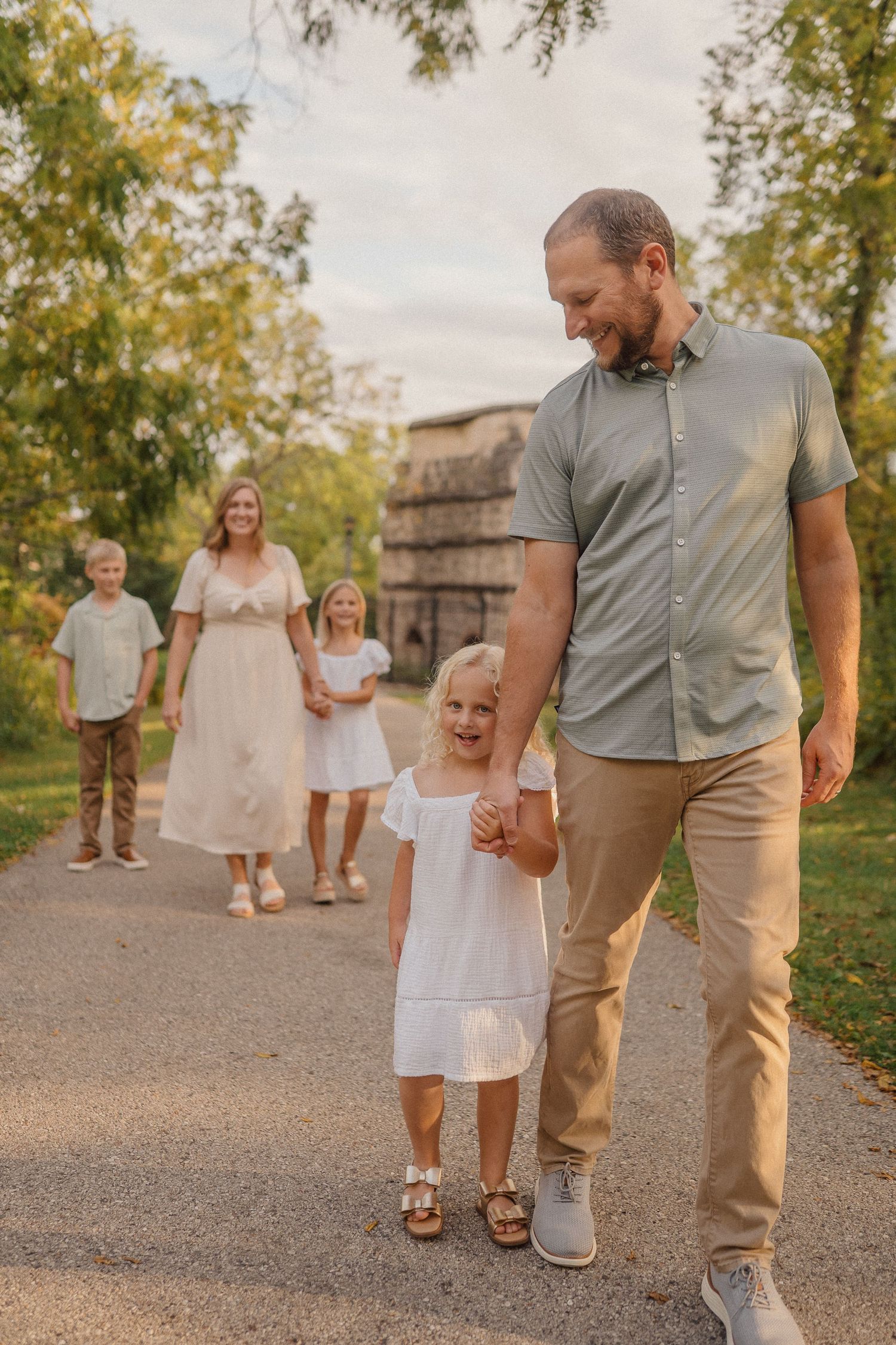 Family walking together on a path at sunset wearing coordinated white and neutral outfits near rustic barn building.