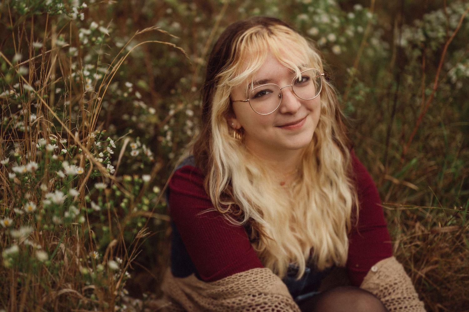 Warm outdoor portrait with someone wearing glasses and a burgundy sweater among autumn foliage.