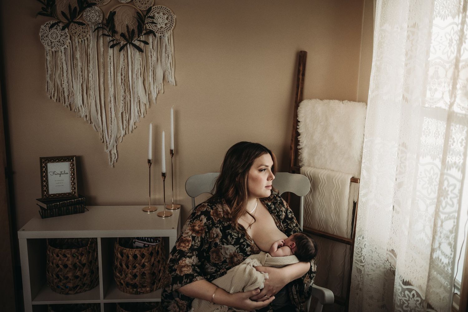 Moody nursery photography with floral dress against white curtains and decorative wall hangings.
