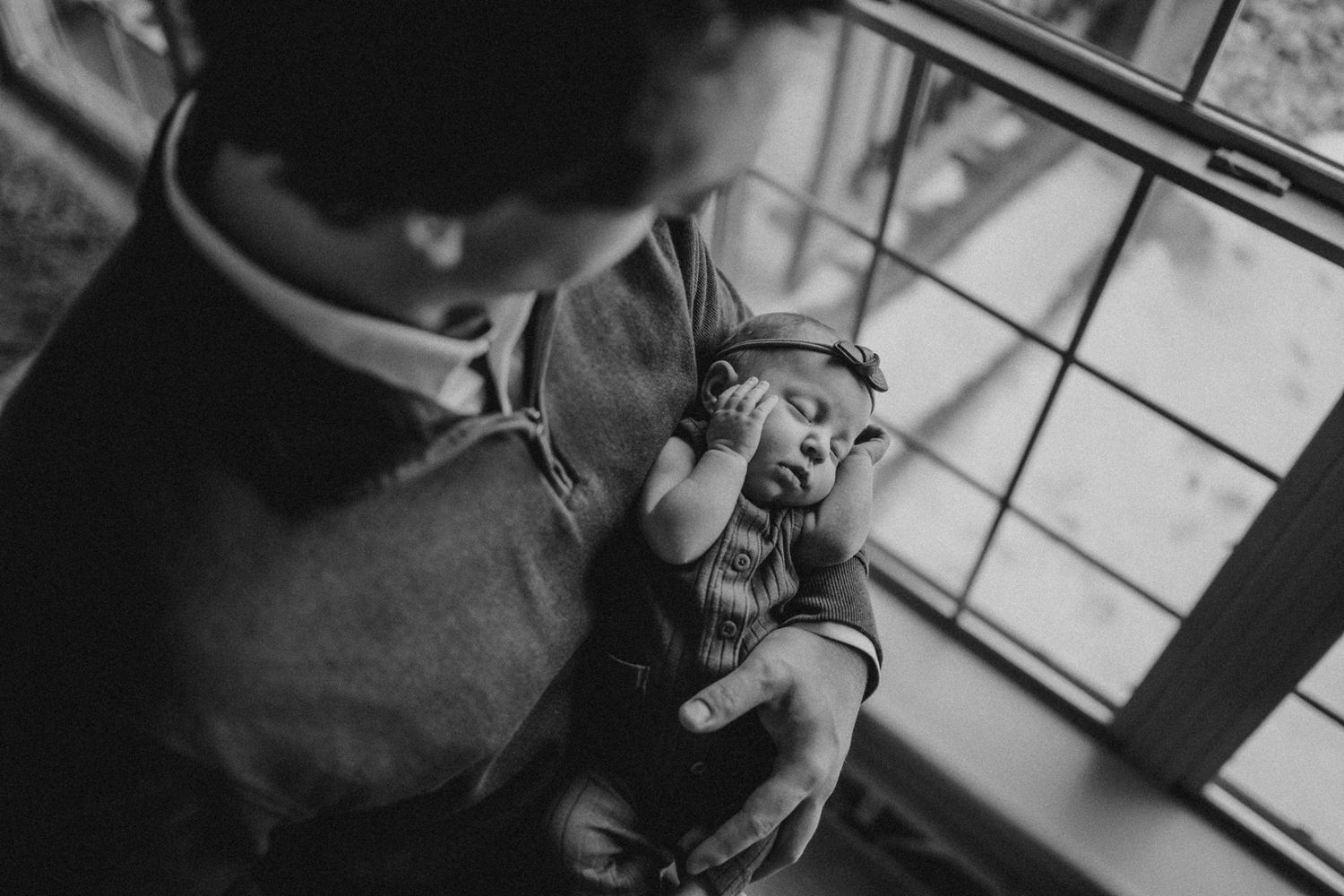 Black and white photo of newborn baby being cradled near window.