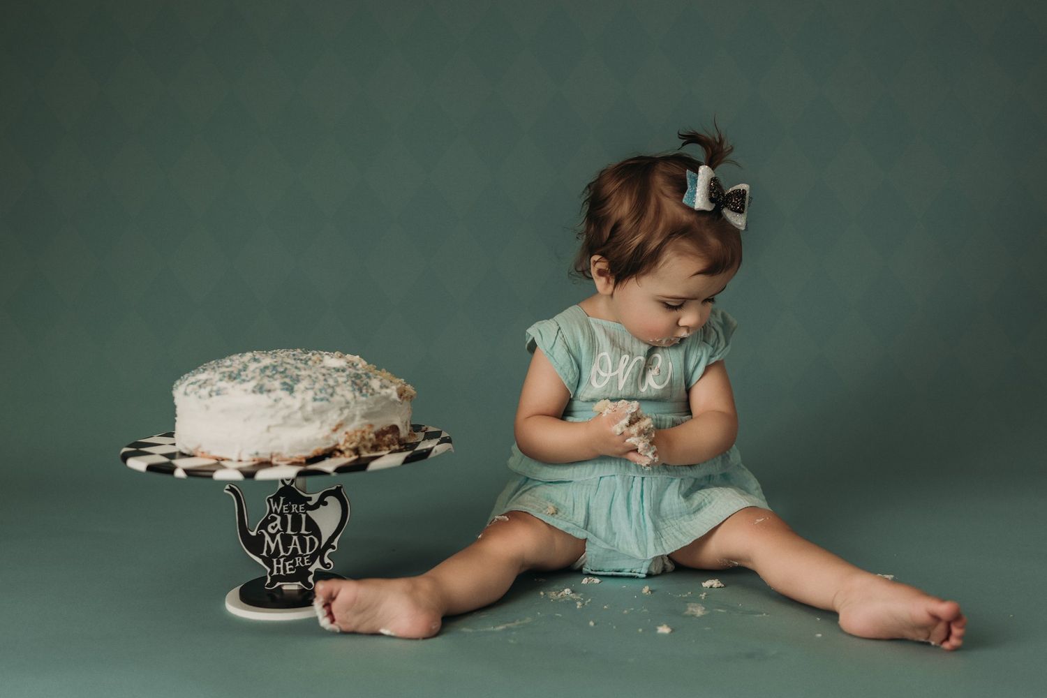 Birthday photoshoot scene with mint dress and decorated cake against dark green background.