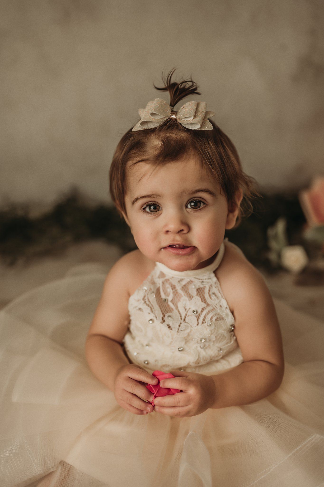 A beautiful portrait features a cream lace dress and bow hairpiece against a neutral background.