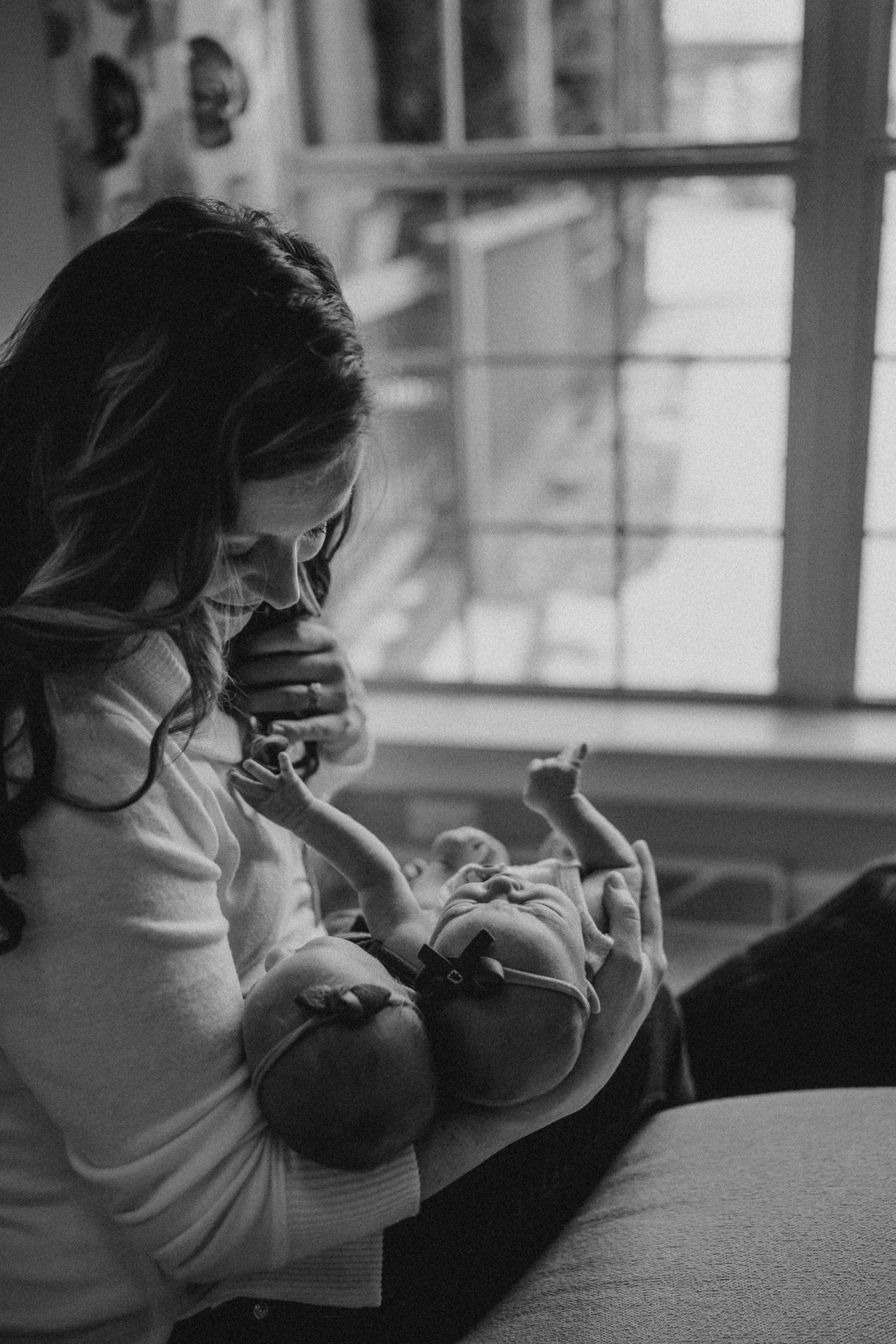 Black and white portrait of parent bonding with newborn by window.
