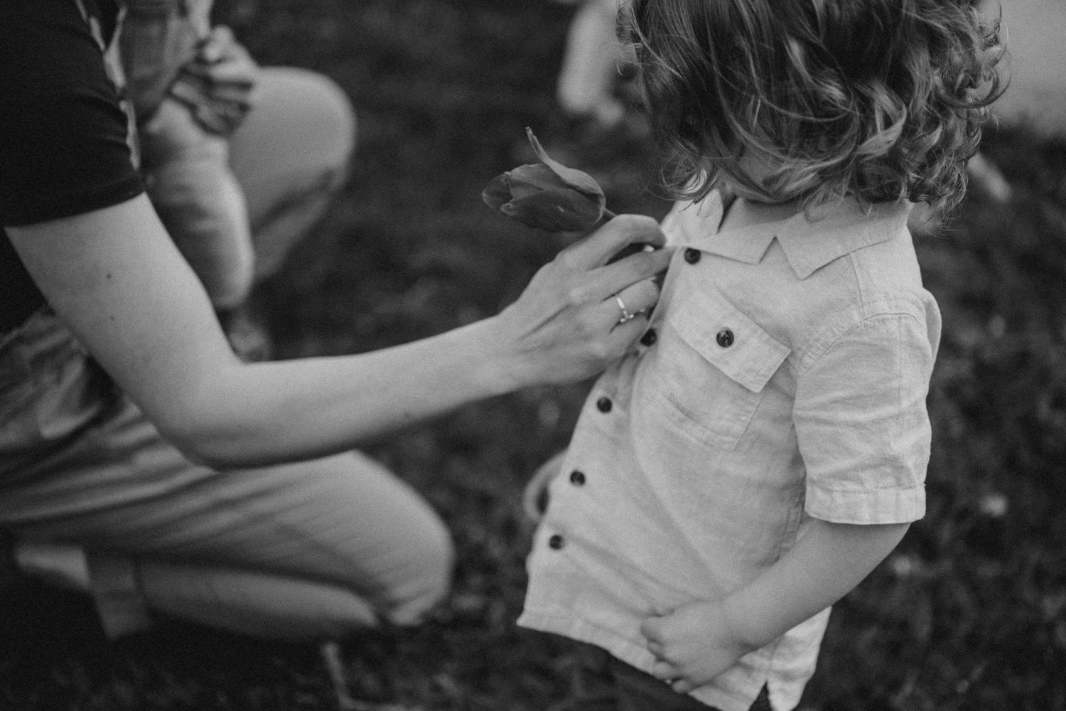 A black and white candid photo showing someone adjusting a child's shirt outdoors.