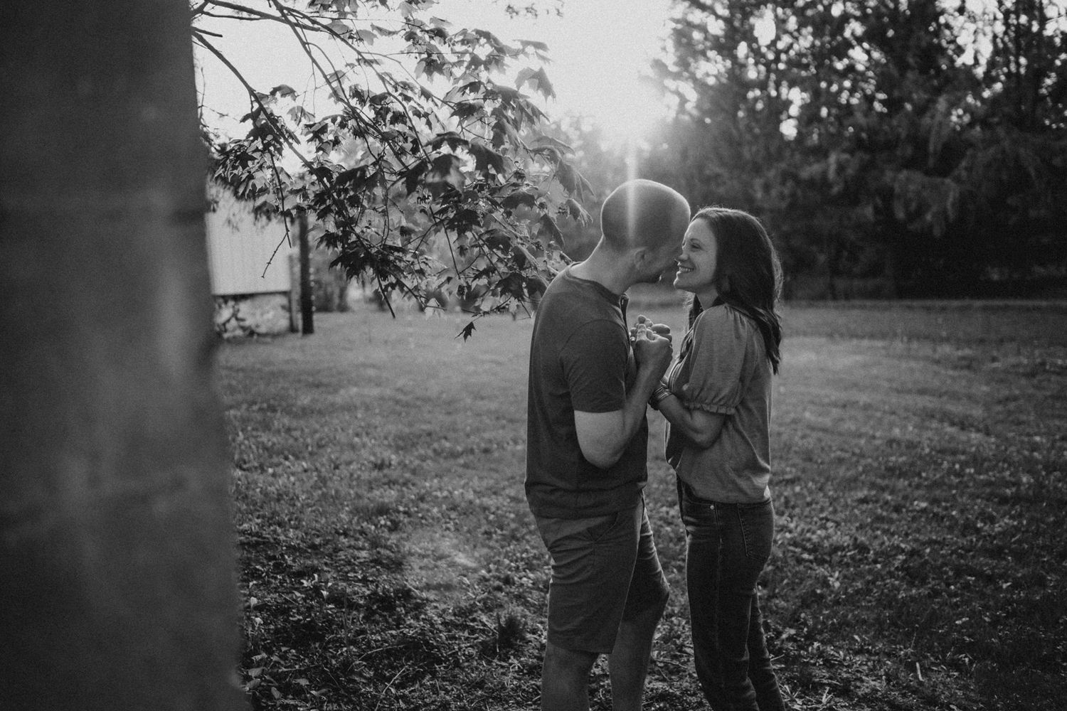 A romantic black and white silhouette photo of a couple embracing in a sunlit garden setting.