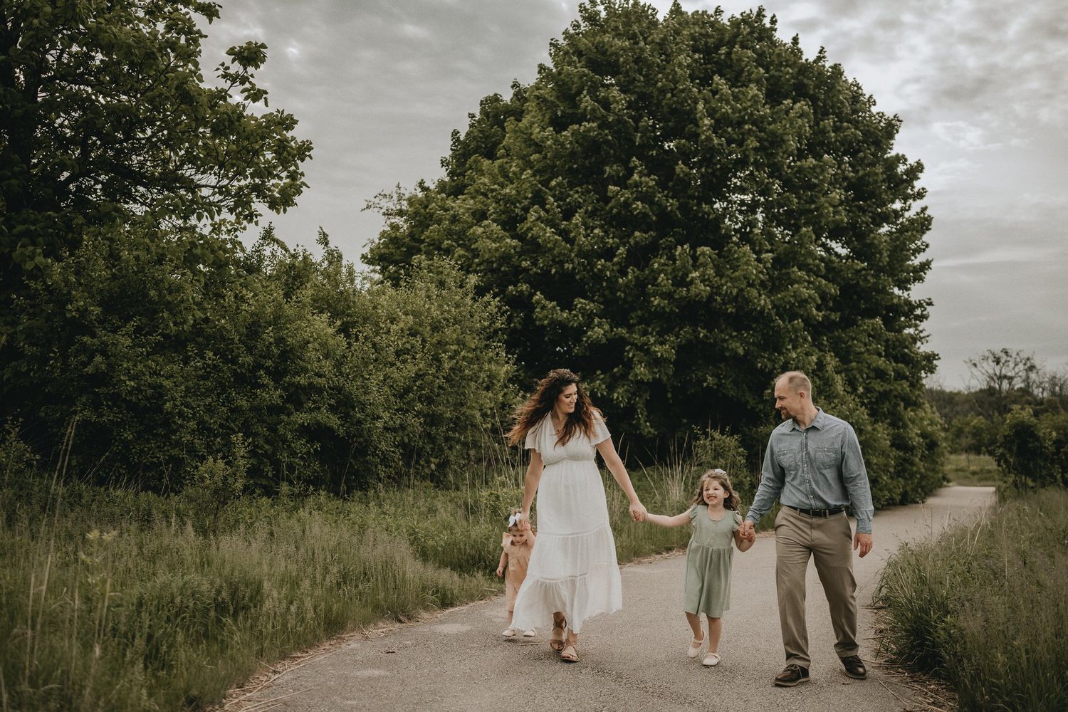 A family walks hand-in-hand down a winding nature path on a summer evening.