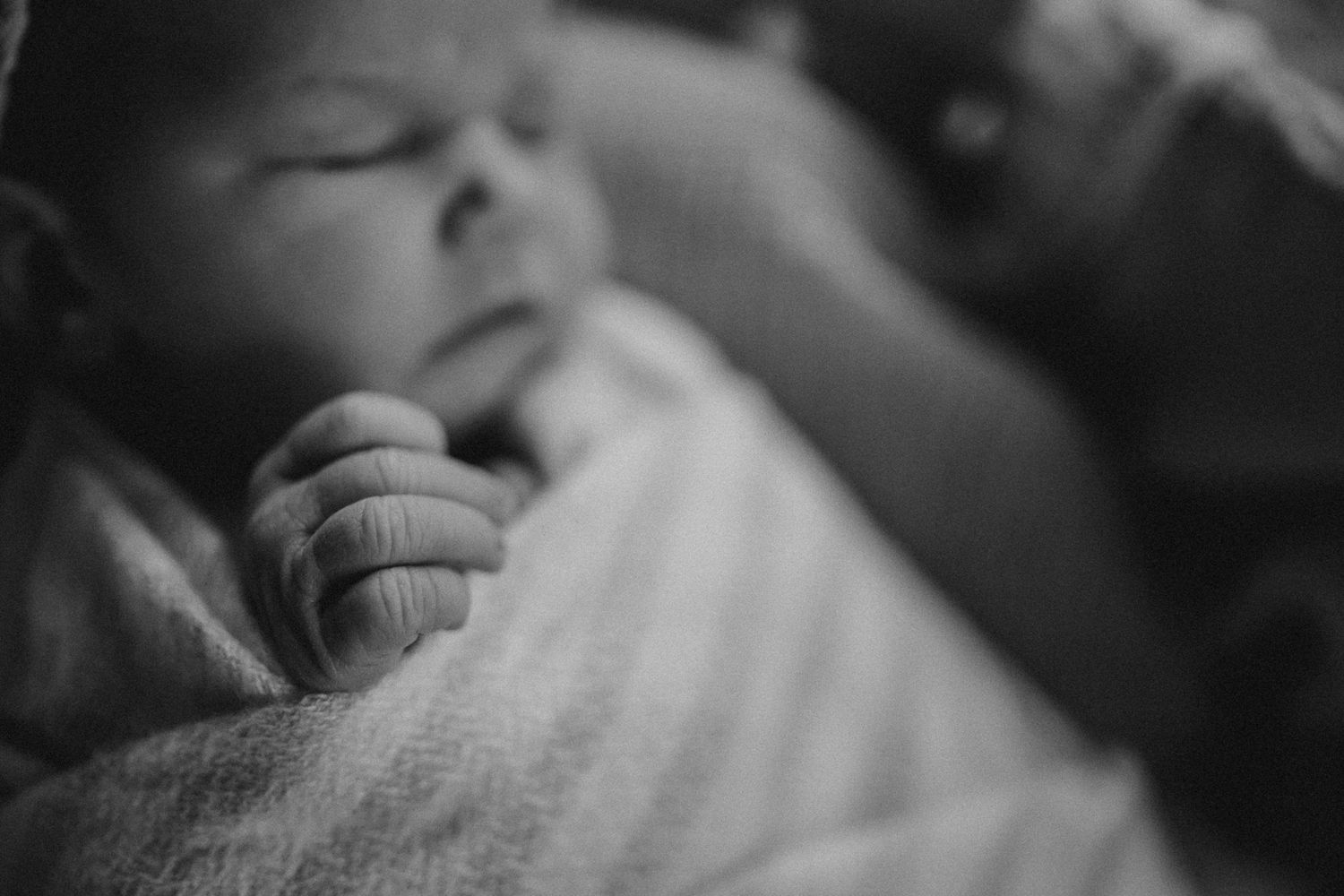 Artistic black and white close-up of sleeping infant's tiny hand and wrapped body.