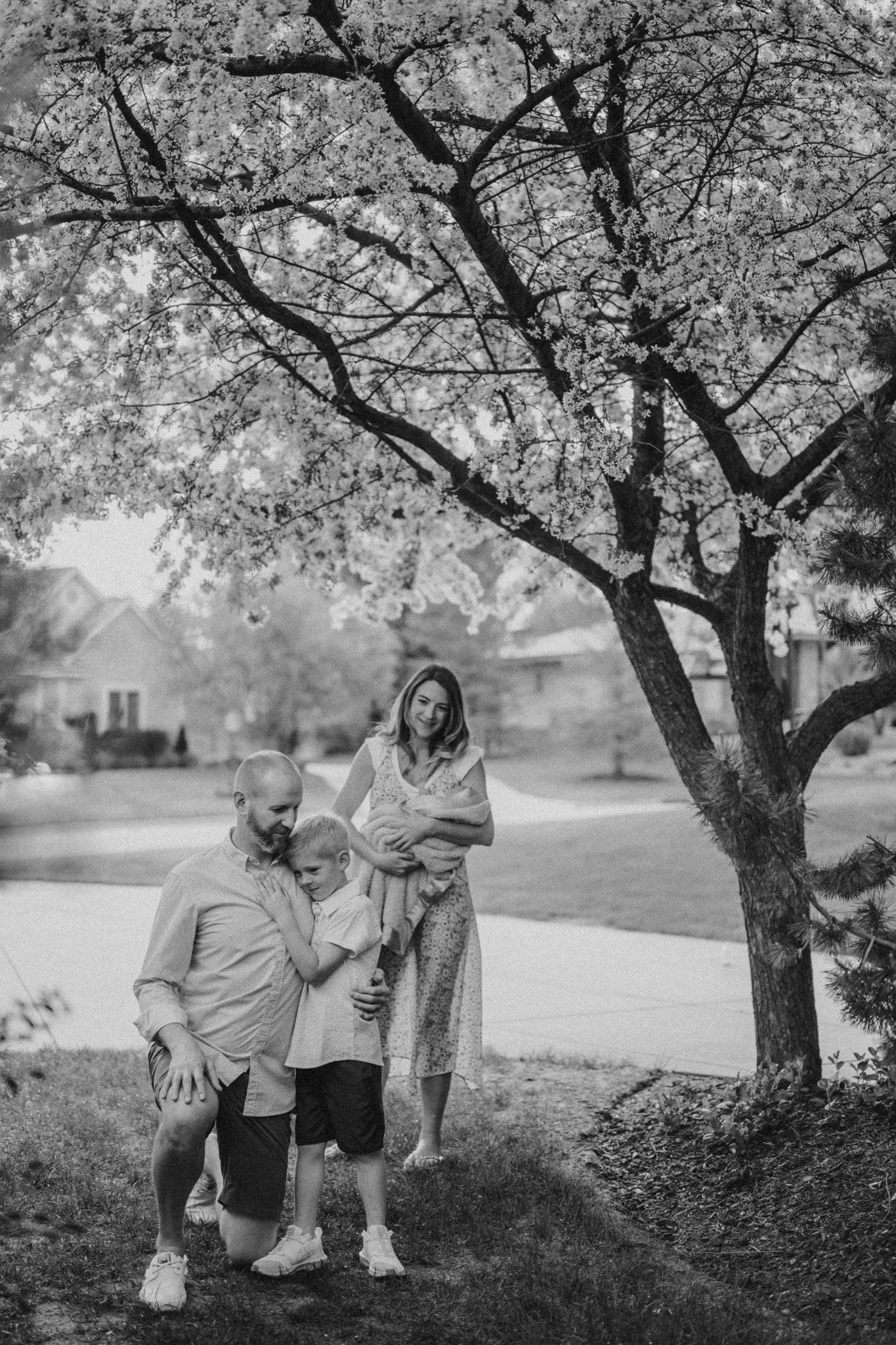 Family poses under a blooming cherry tree in a peaceful park setting.