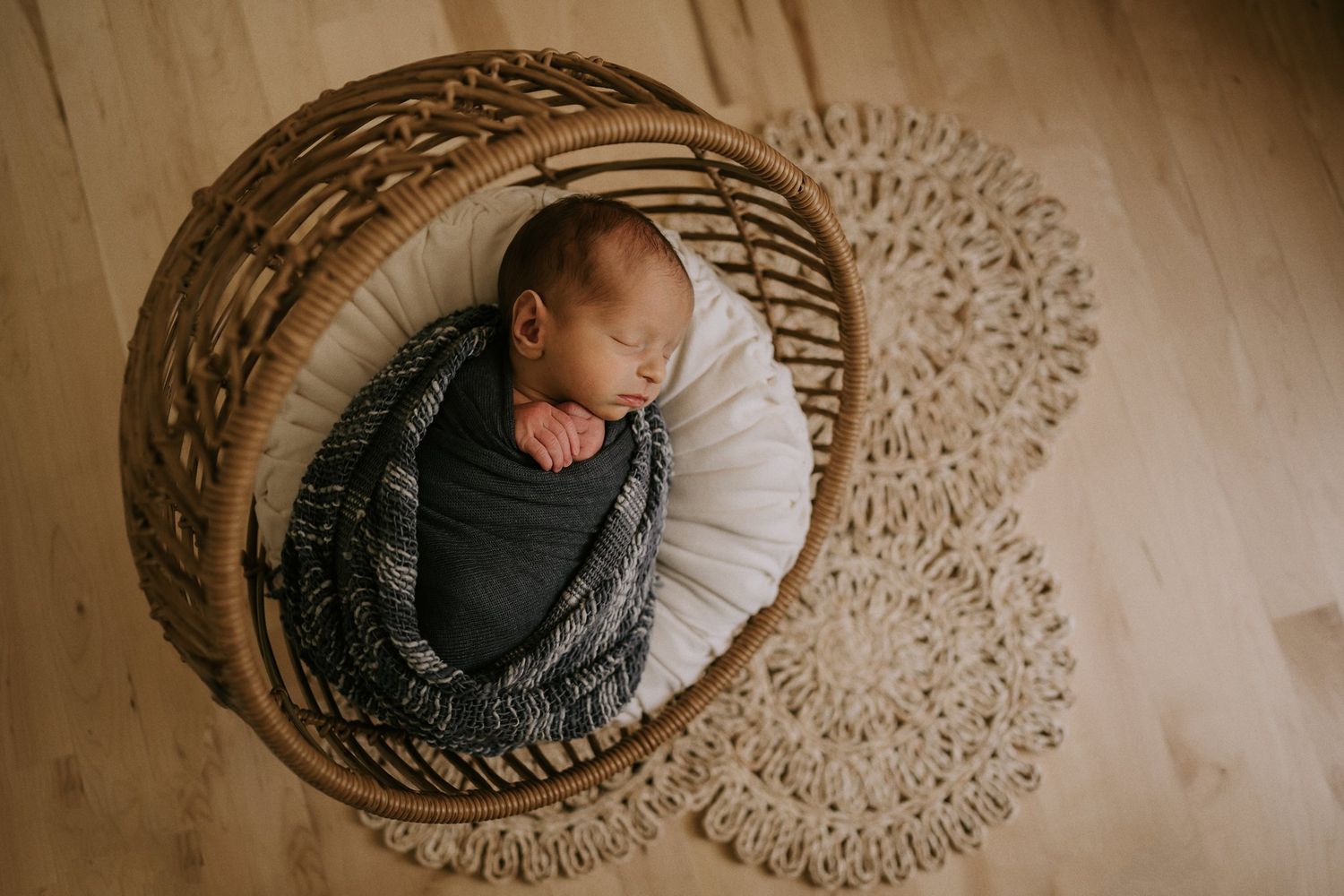 Overhead view of a sleeping newborn in a woven basket casting intricate shadows.
