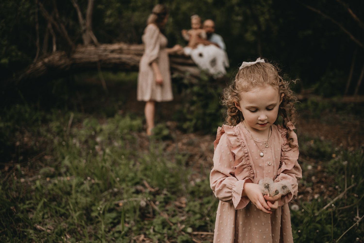 A young child in a pink vintage dress explores nature in a moody forest setting.