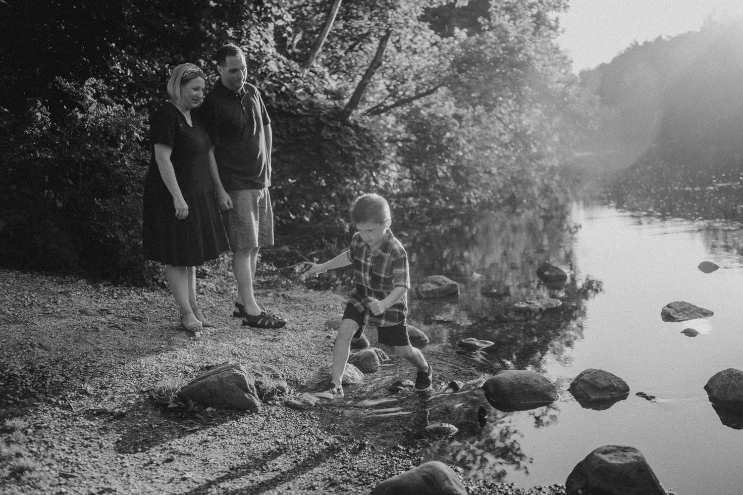 Family enjoying a peaceful moment by a rocky riverside in black and white photography.