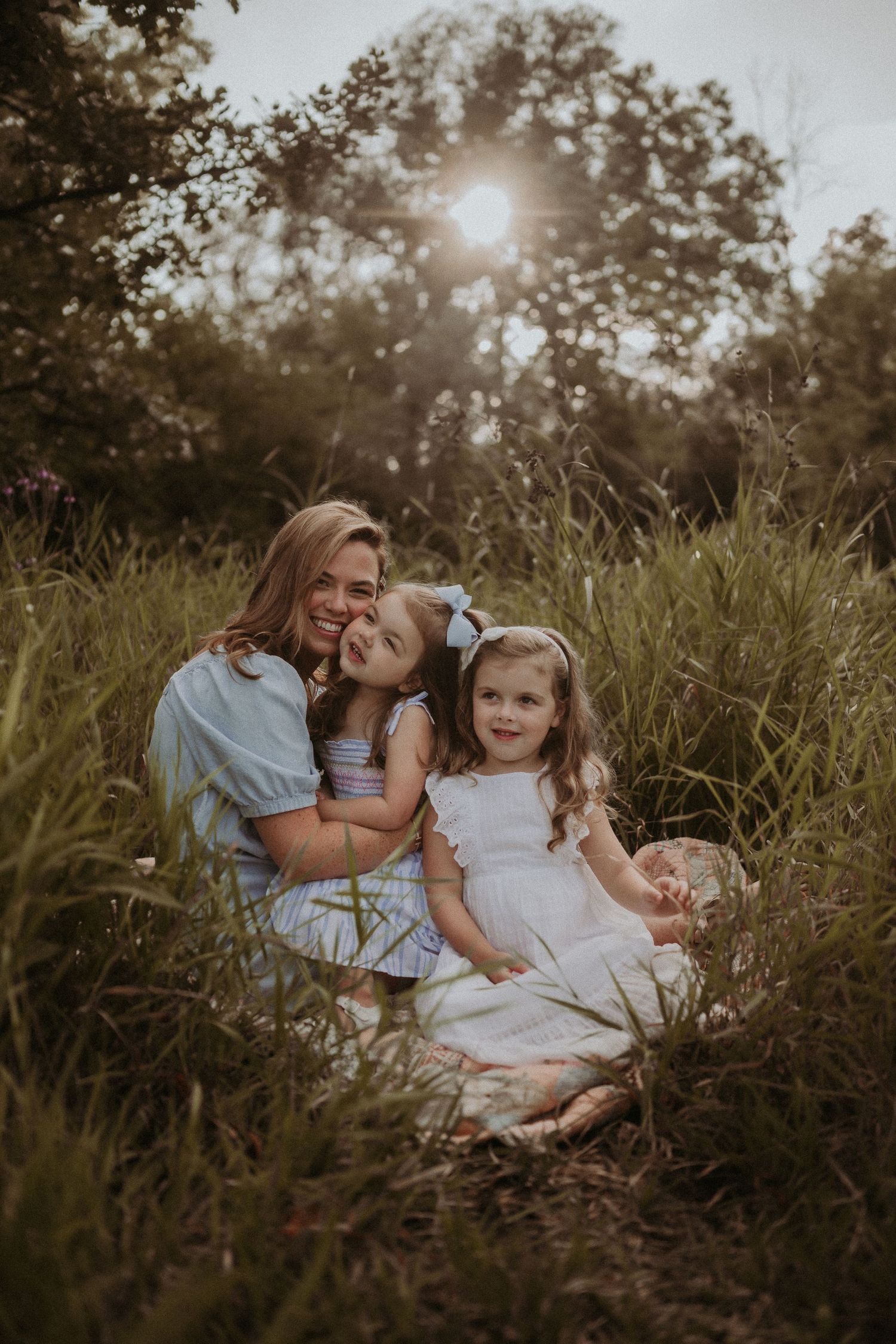 Intimate family portrait with sun flare through trees in tall grass field.