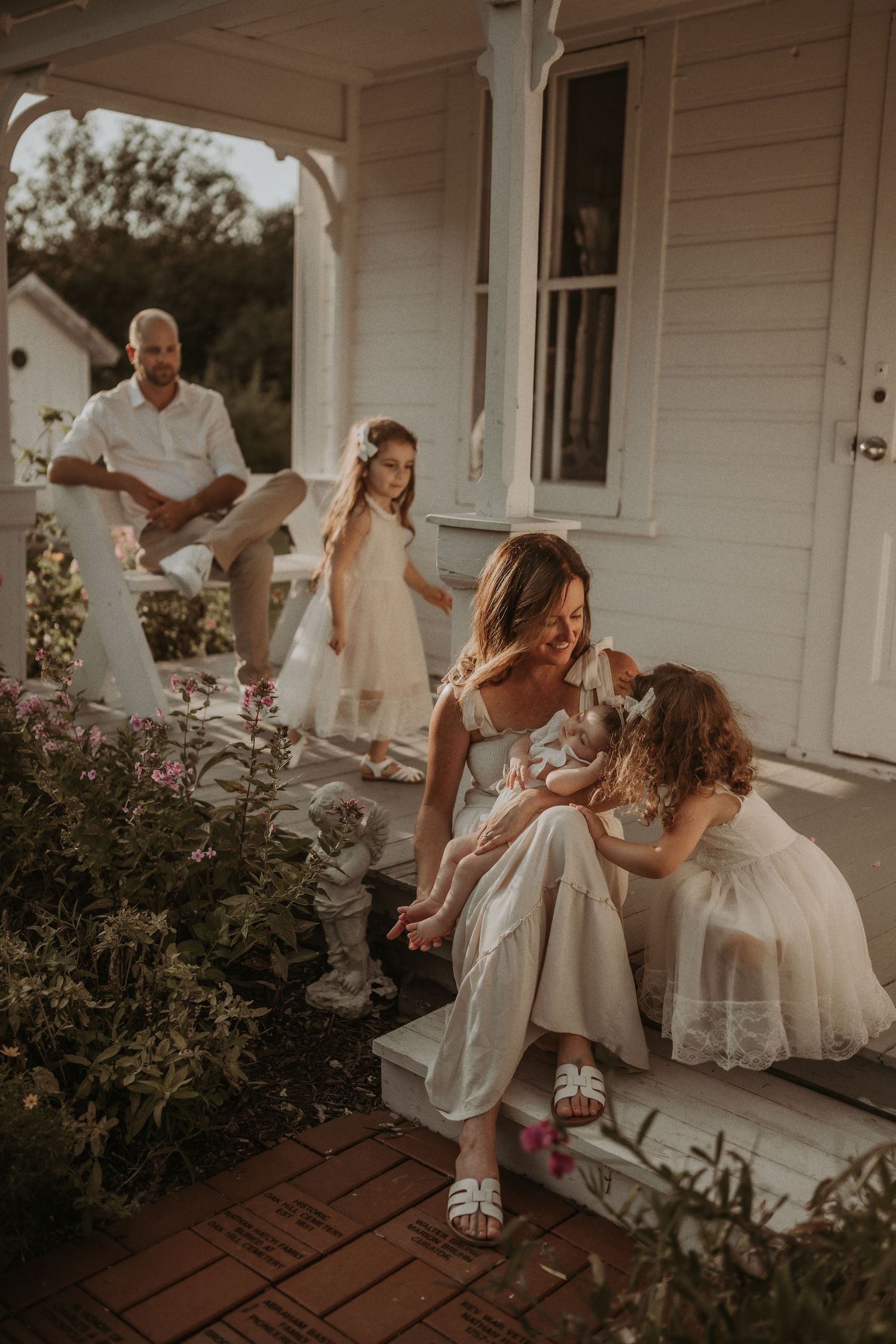 A warm evening family portrait on a white farmhouse porch surrounded by blooming flowers.
