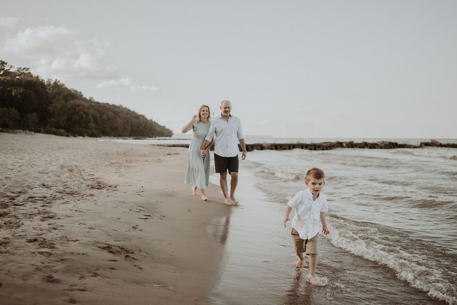 Three people walking along the beach shoreline during a moody sunset.