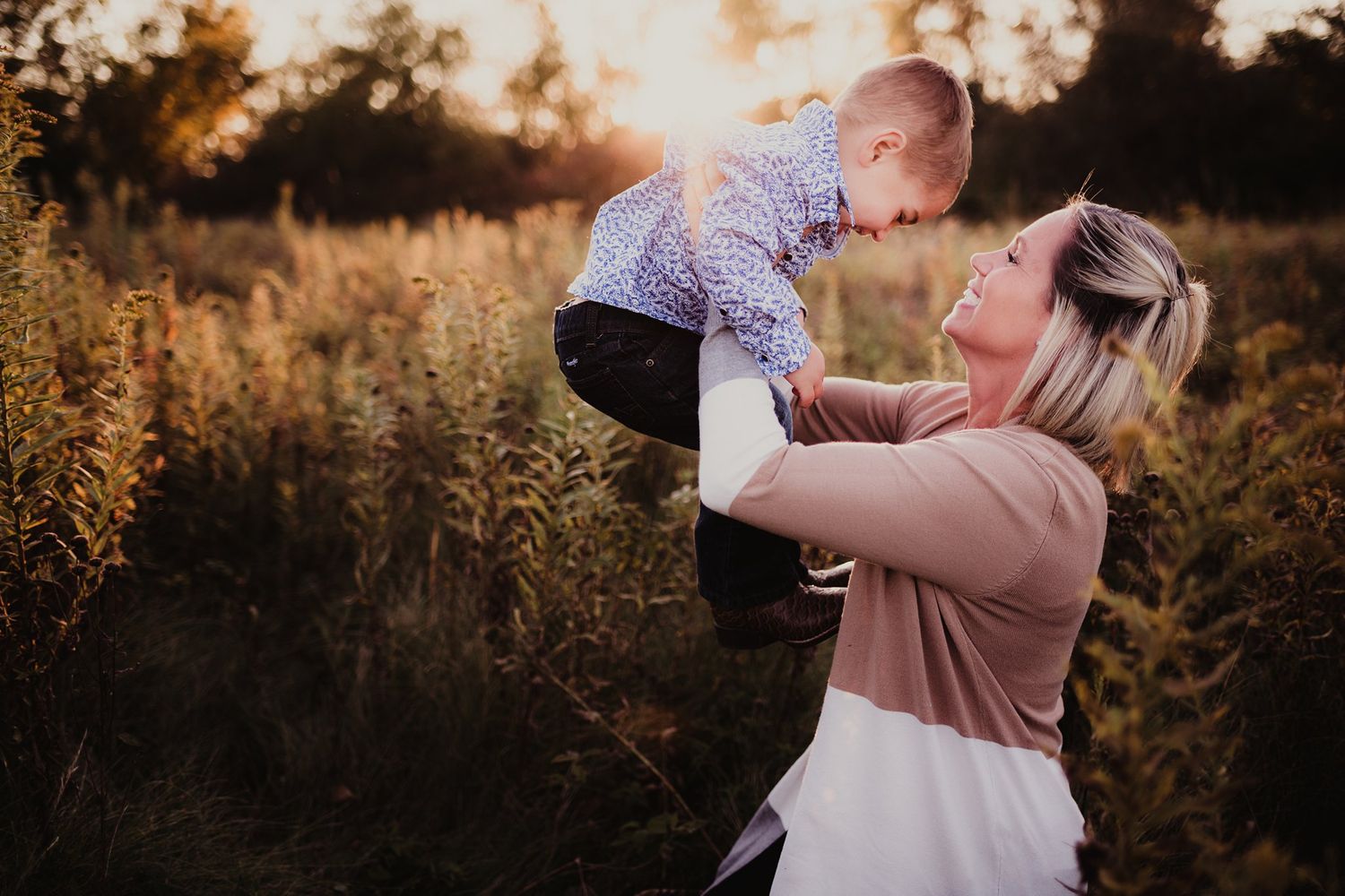 Playful moment between adult and small child lifting up in field at sunset.