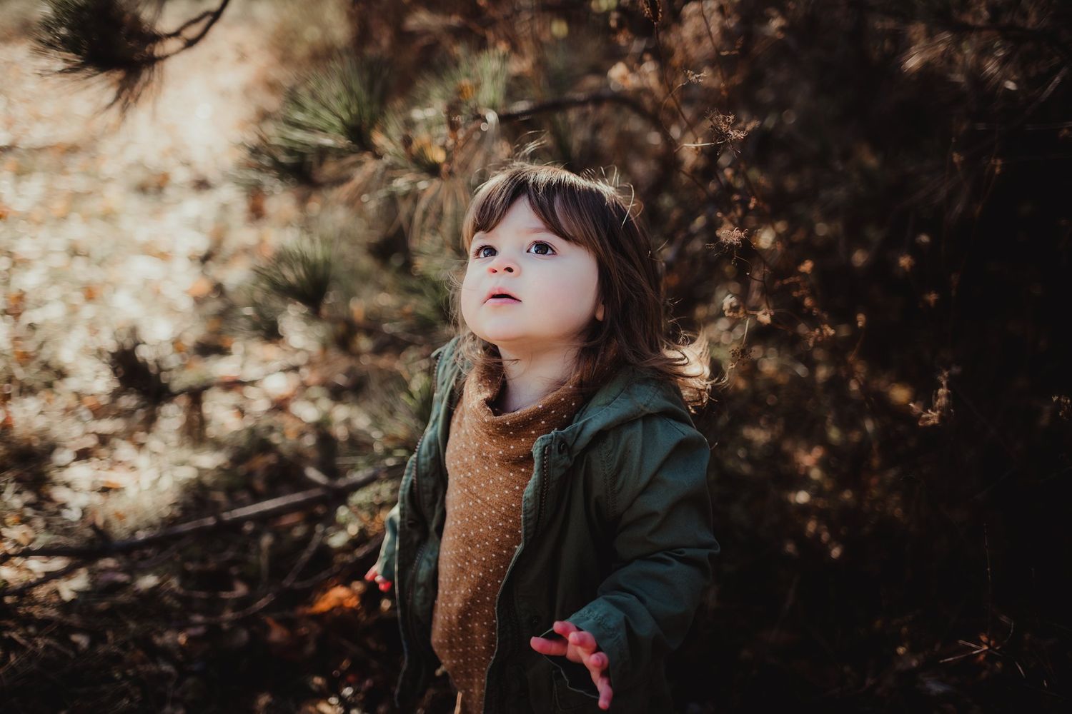 A small child in outdoor clothing looks up with wonder against a blurred natural background.