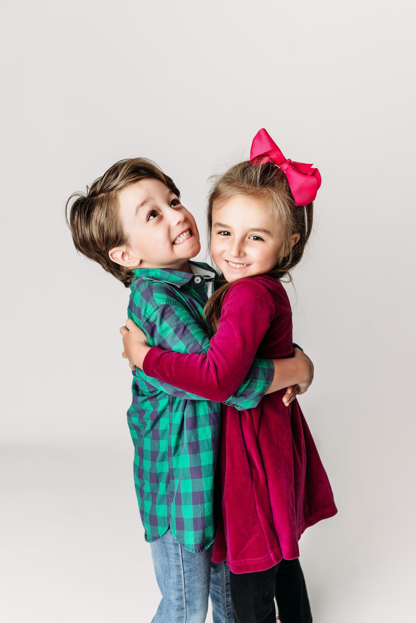 Two children in festive outfits share warm embrace against white background.