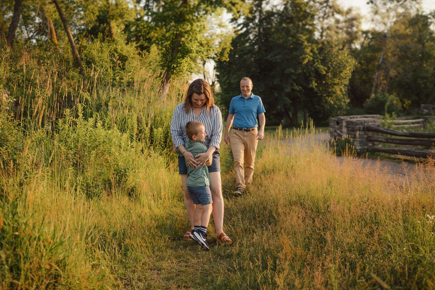 Family walks together through tall grass during golden hour.