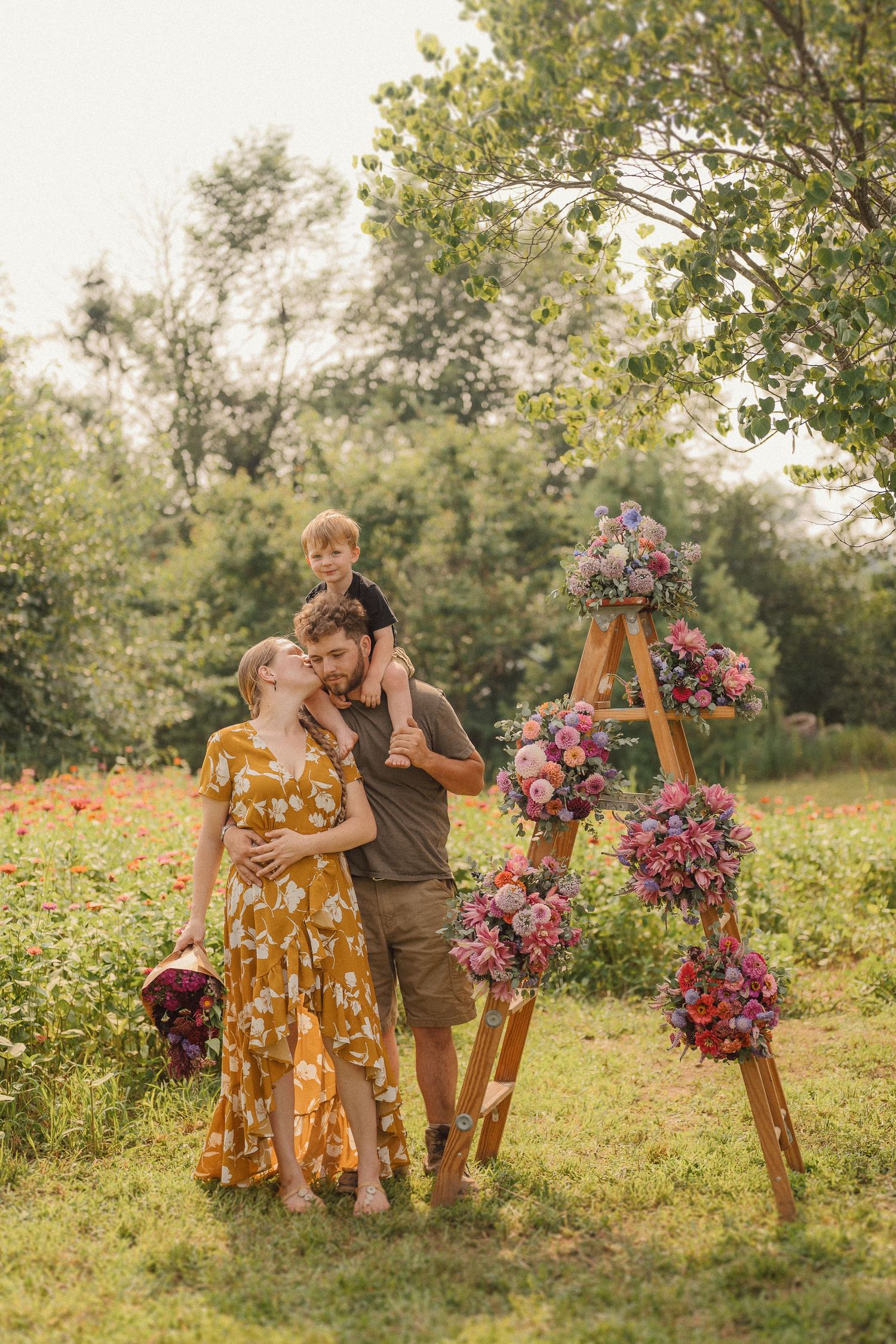 An outdoor family portrait next to a wooden ladder decorated with vibrant pink and purple floral arrangements at sunset.