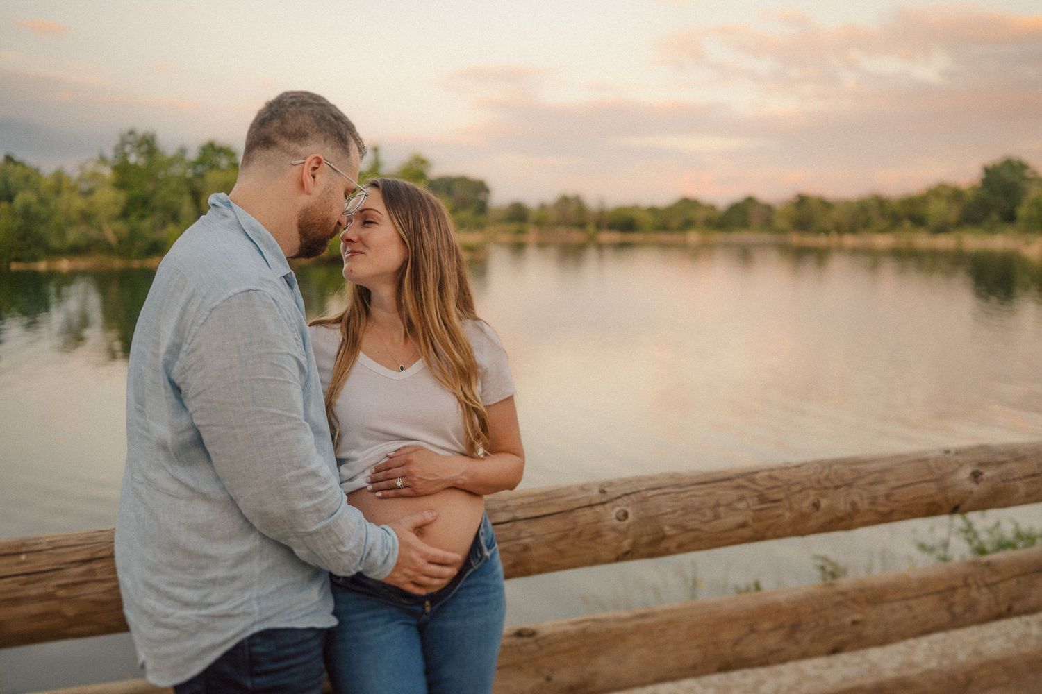 Sunset maternity photos of couple embracing by waterfront with warm golden light.