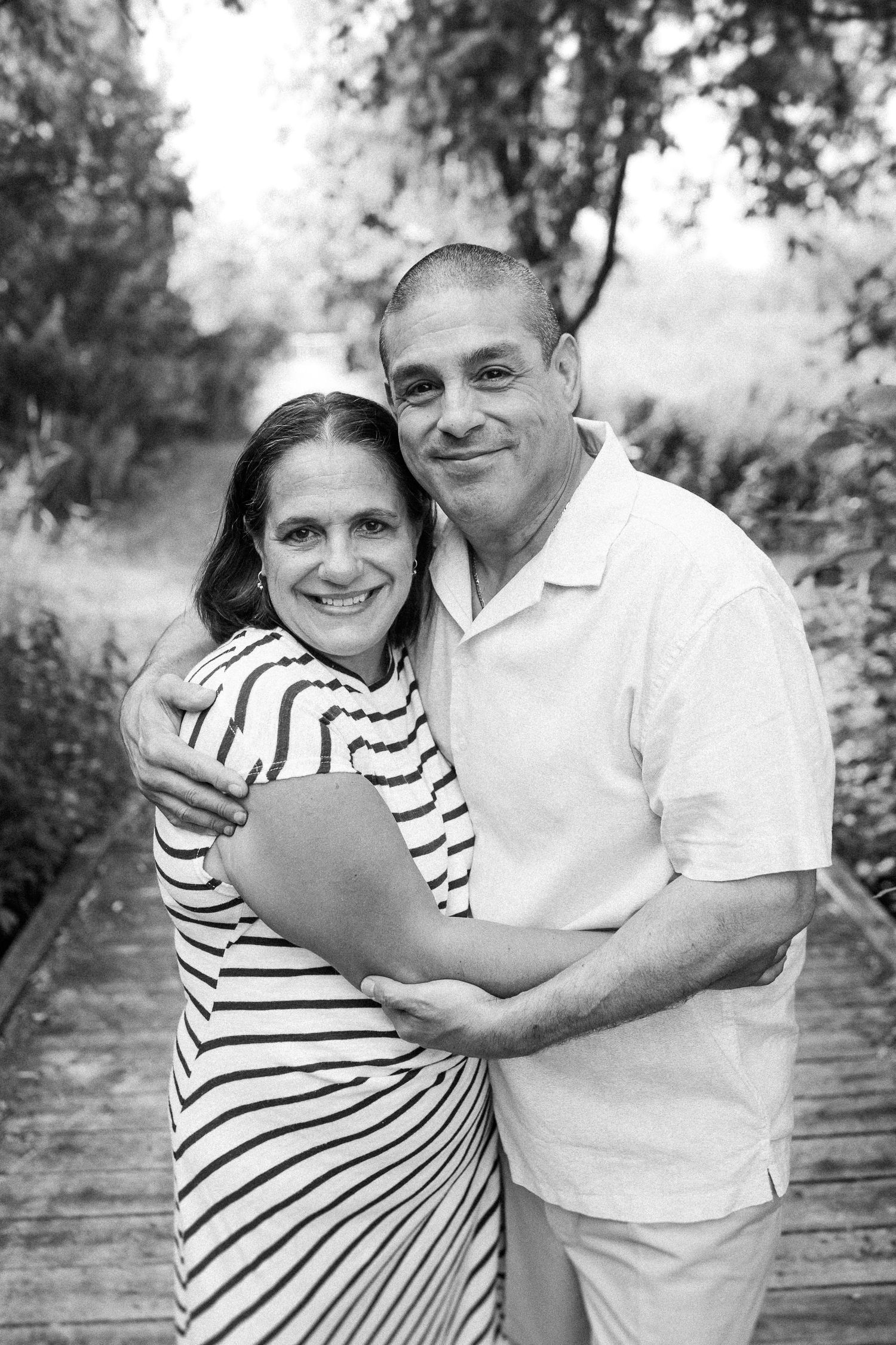 Loving couple in black and white sharing embraces on wooden walkway, with woman in striped shirt and man in white.