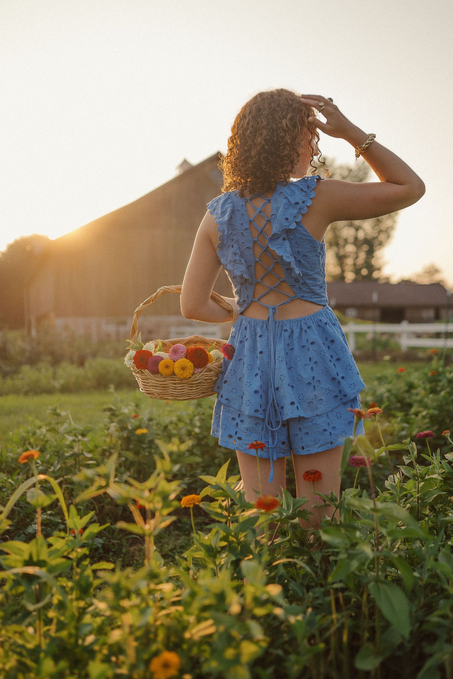 A child in a blue ruffled dress carries a wicker basket through a summer garden at sunset.