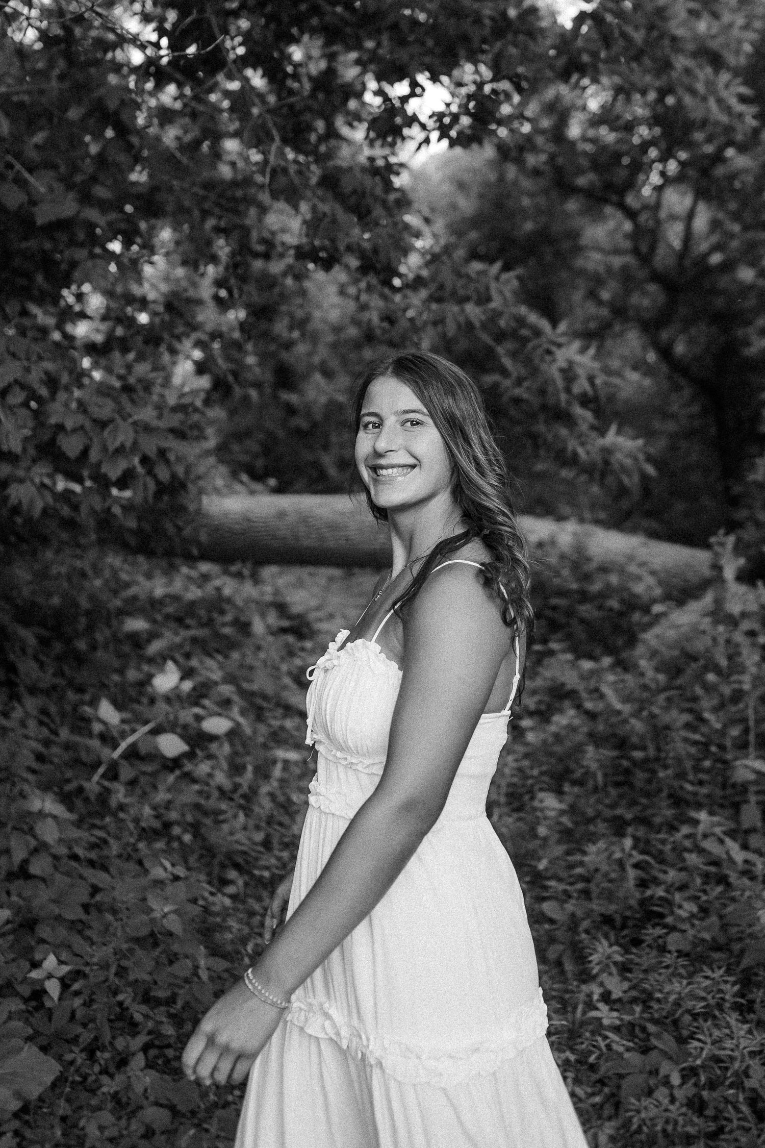 Black and white outdoor portrait of someone wearing a white lace dress in a natural garden setting.