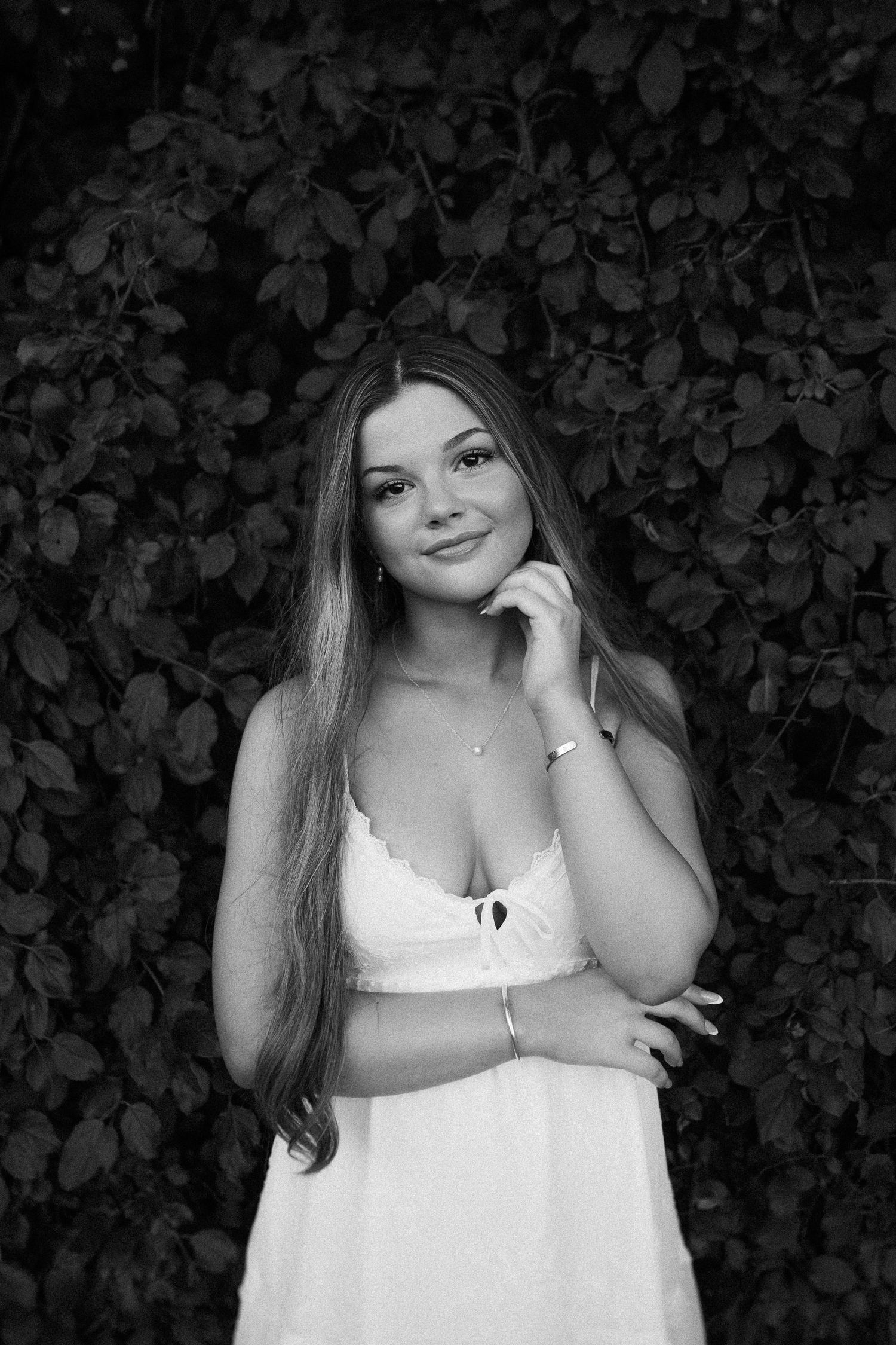 Elegant black and white portrait against leafy backdrop wearing white summer dress.