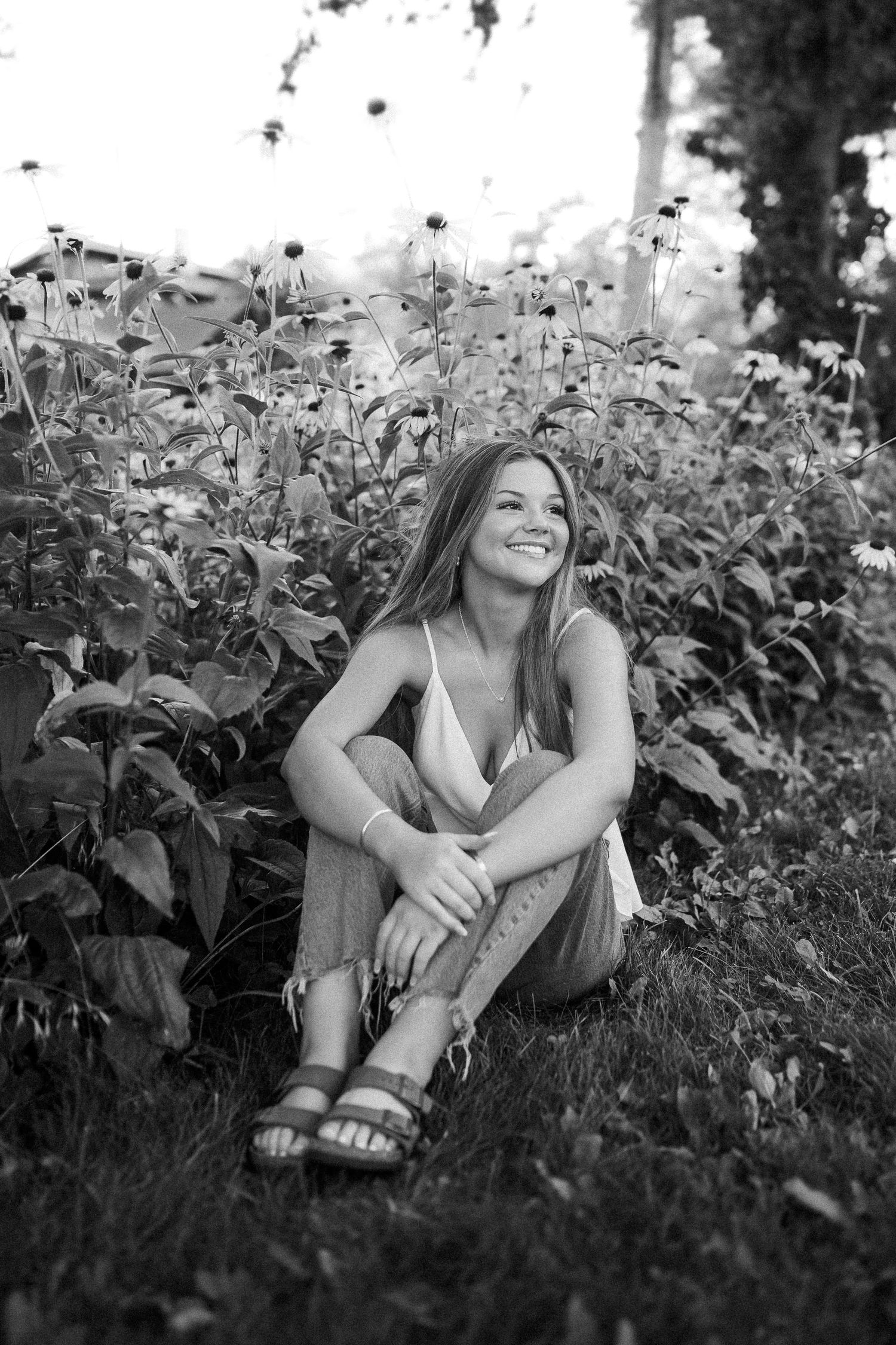 Person sitting relaxed in a garden among leafy plants, captured in black and white photography.
