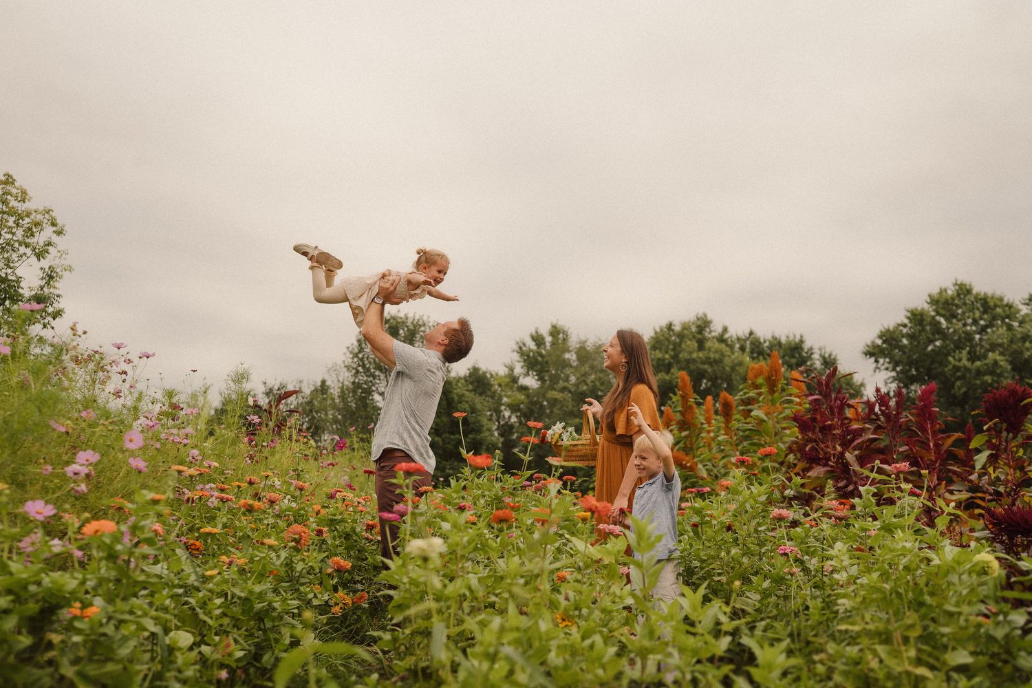 Family plays together in a vibrant garden filled with colorful flowers on an overcast summer day.