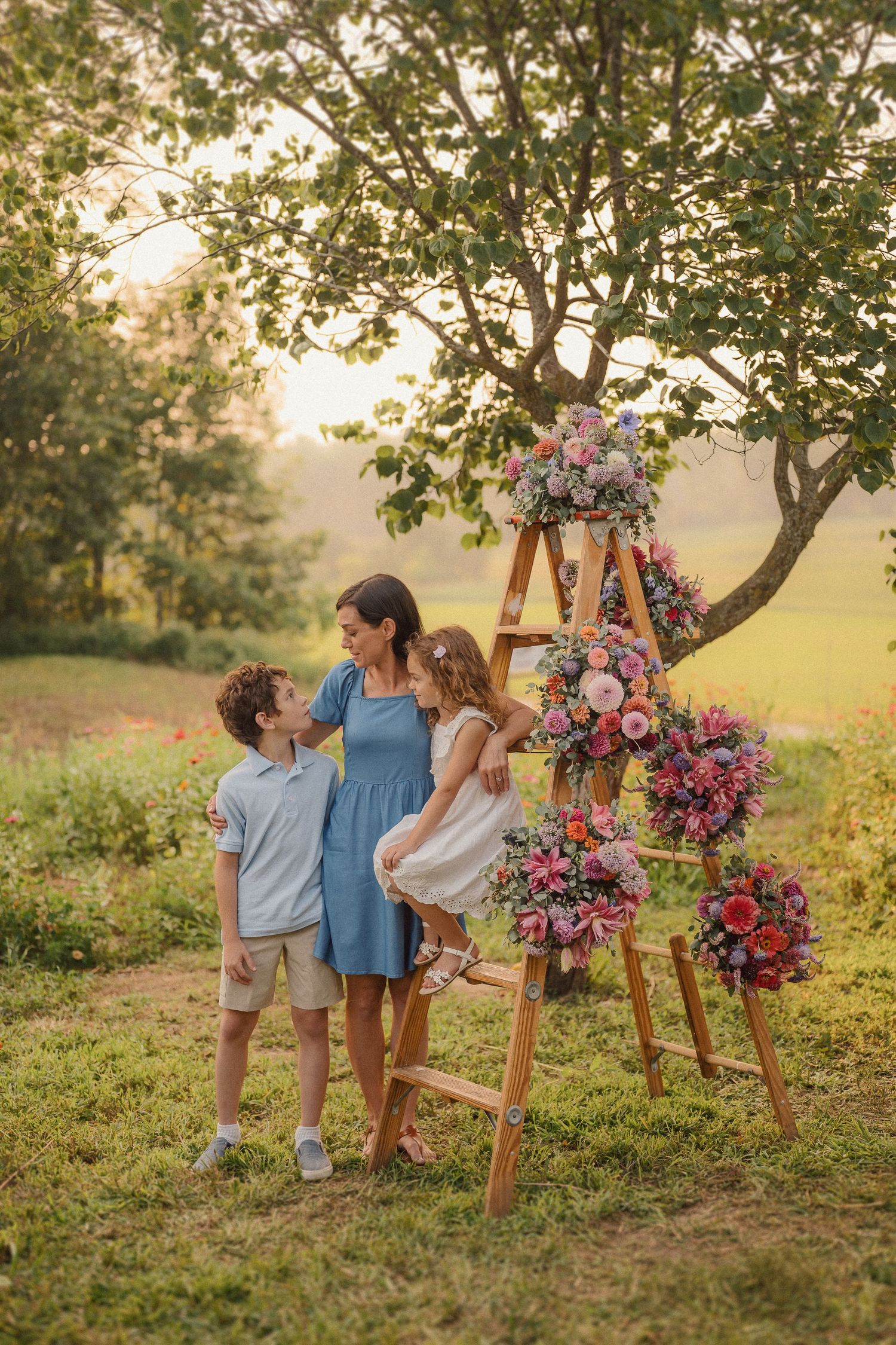 A rustic outdoor photoshoot setup with a wooden ladder adorned with colorful pink and purple floral arrangements.