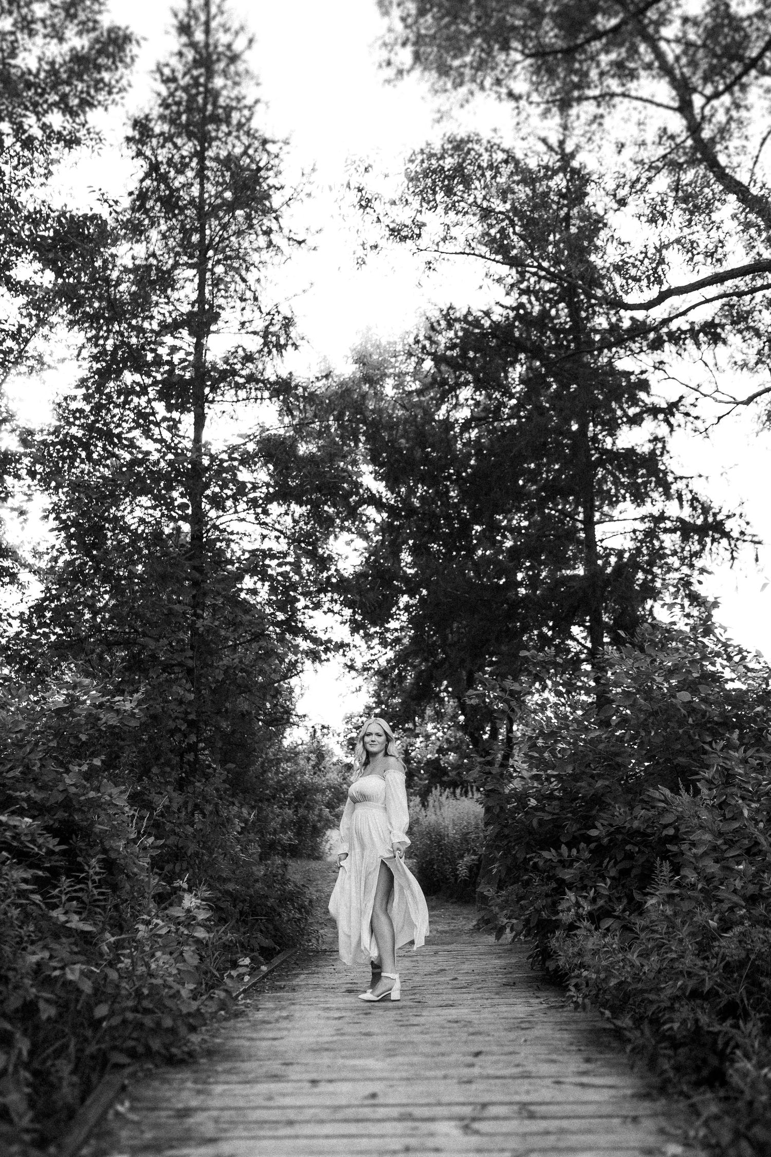 Two figures walk along a tree-lined path in black and white.