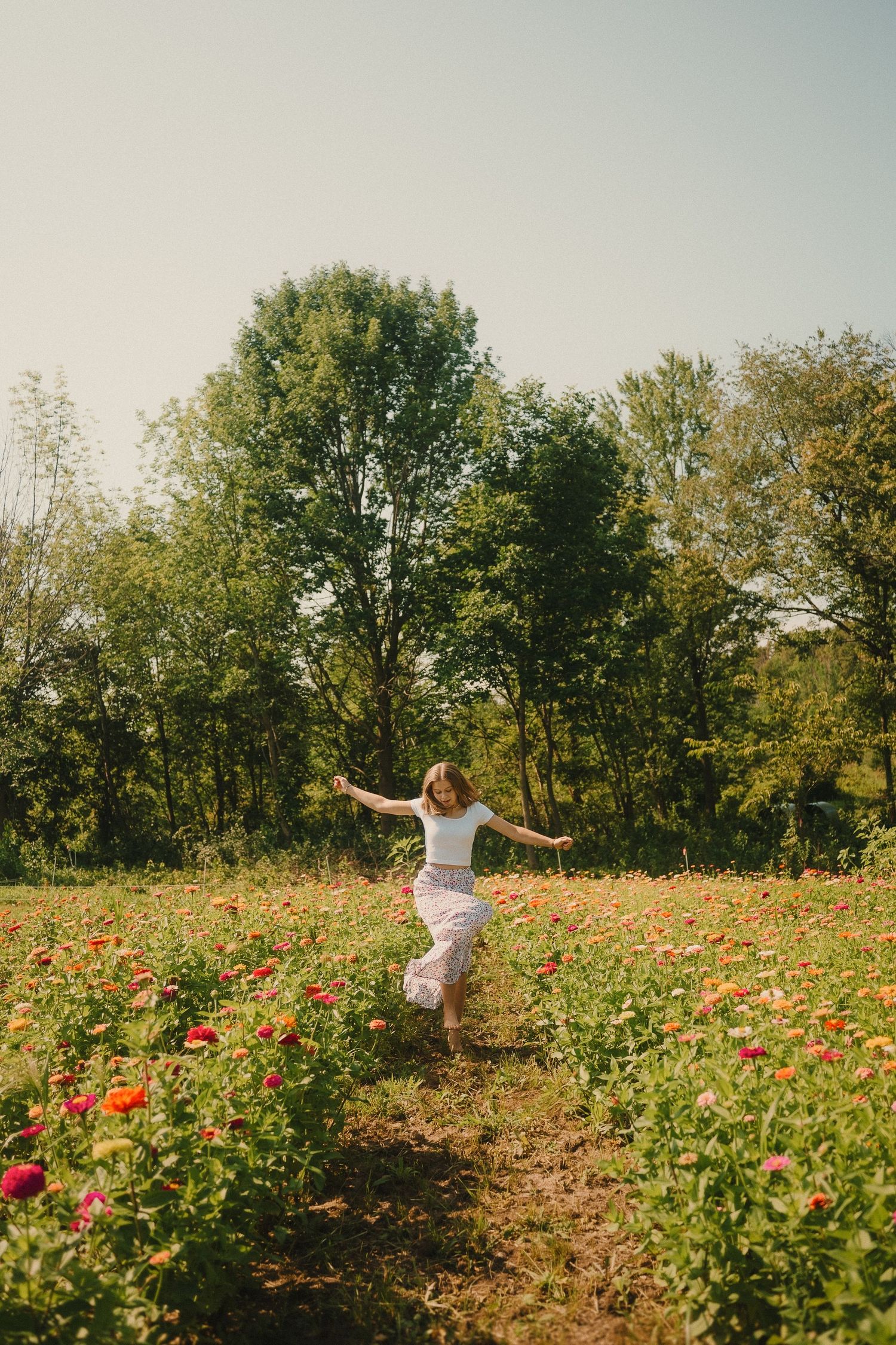 Someone dancing joyfully in a field of vibrant red and orange flowers with trees in the background.