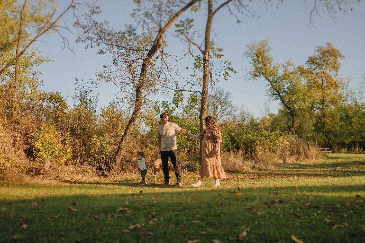 Golden hour family portrait in natural outdoor setting with trees in background.