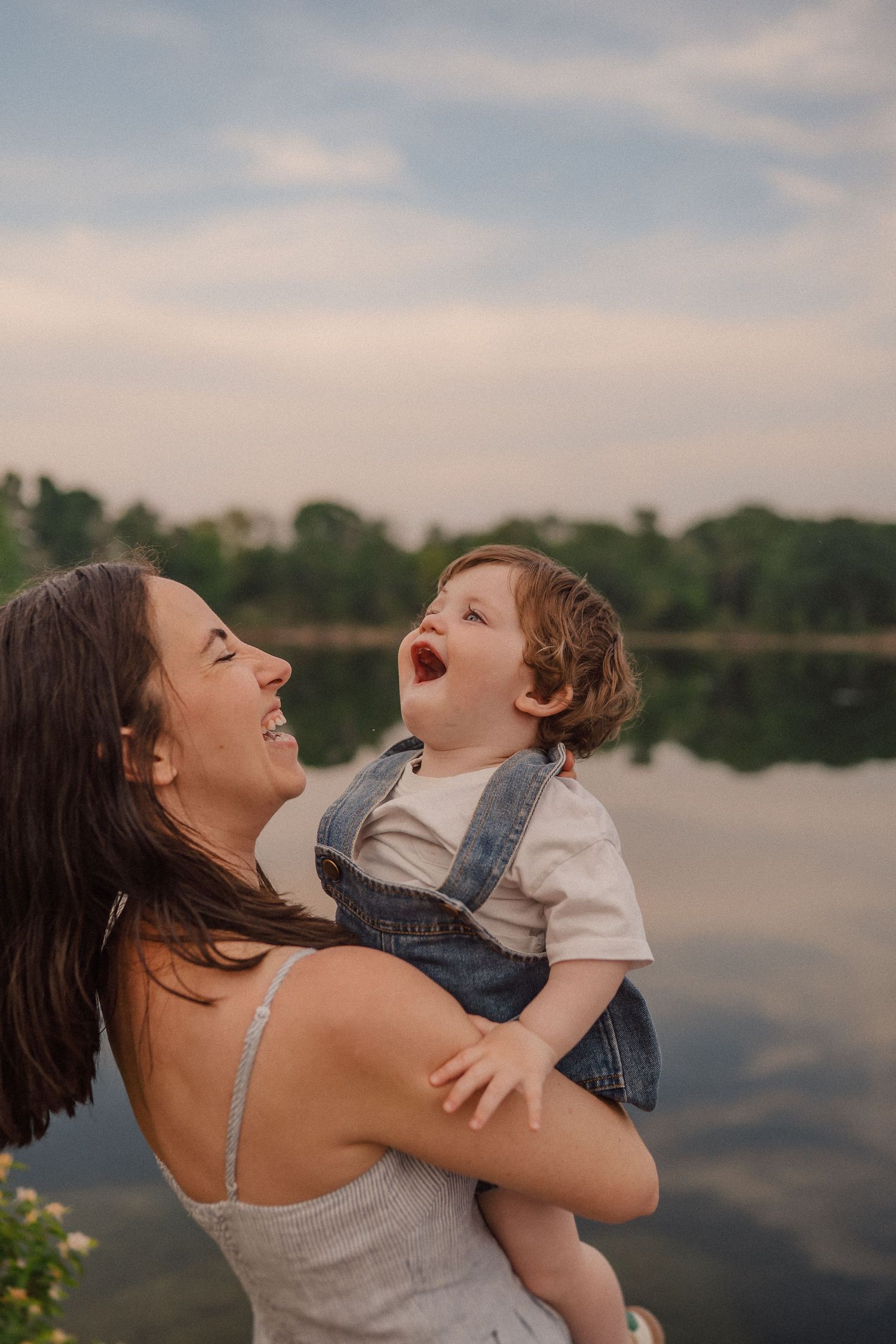 Candid moment of shared laughter against a serene lakeside backdrop at sunset.