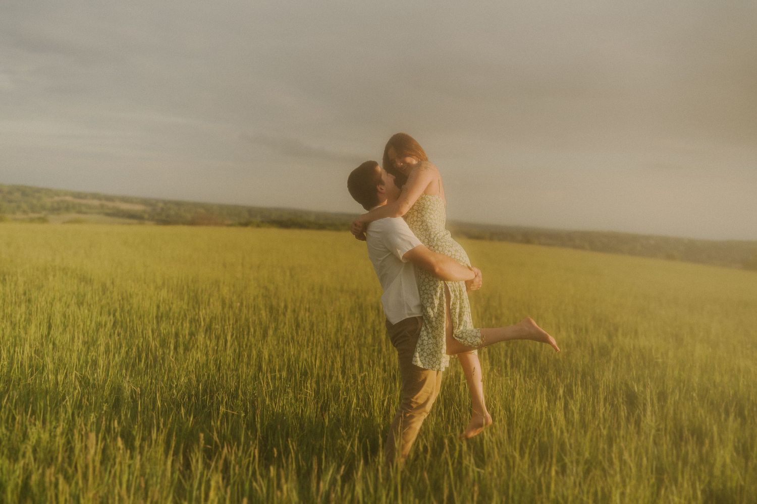 Romantic couple embracing playfully in a golden wheat field during sunset.
