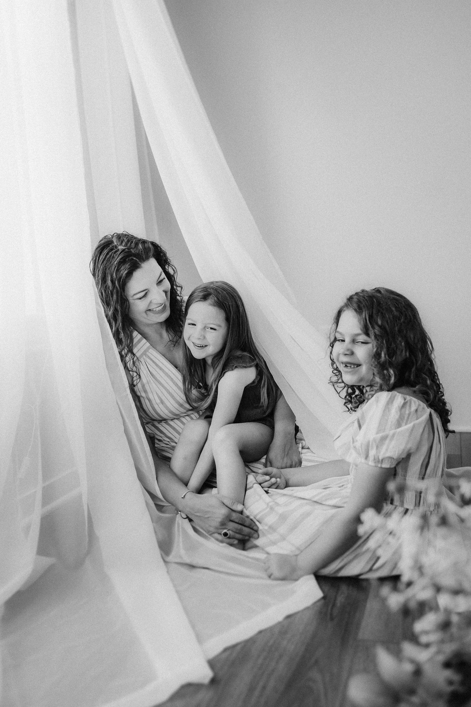 Candid black and white photo showing intimate family moment under draped fabric.