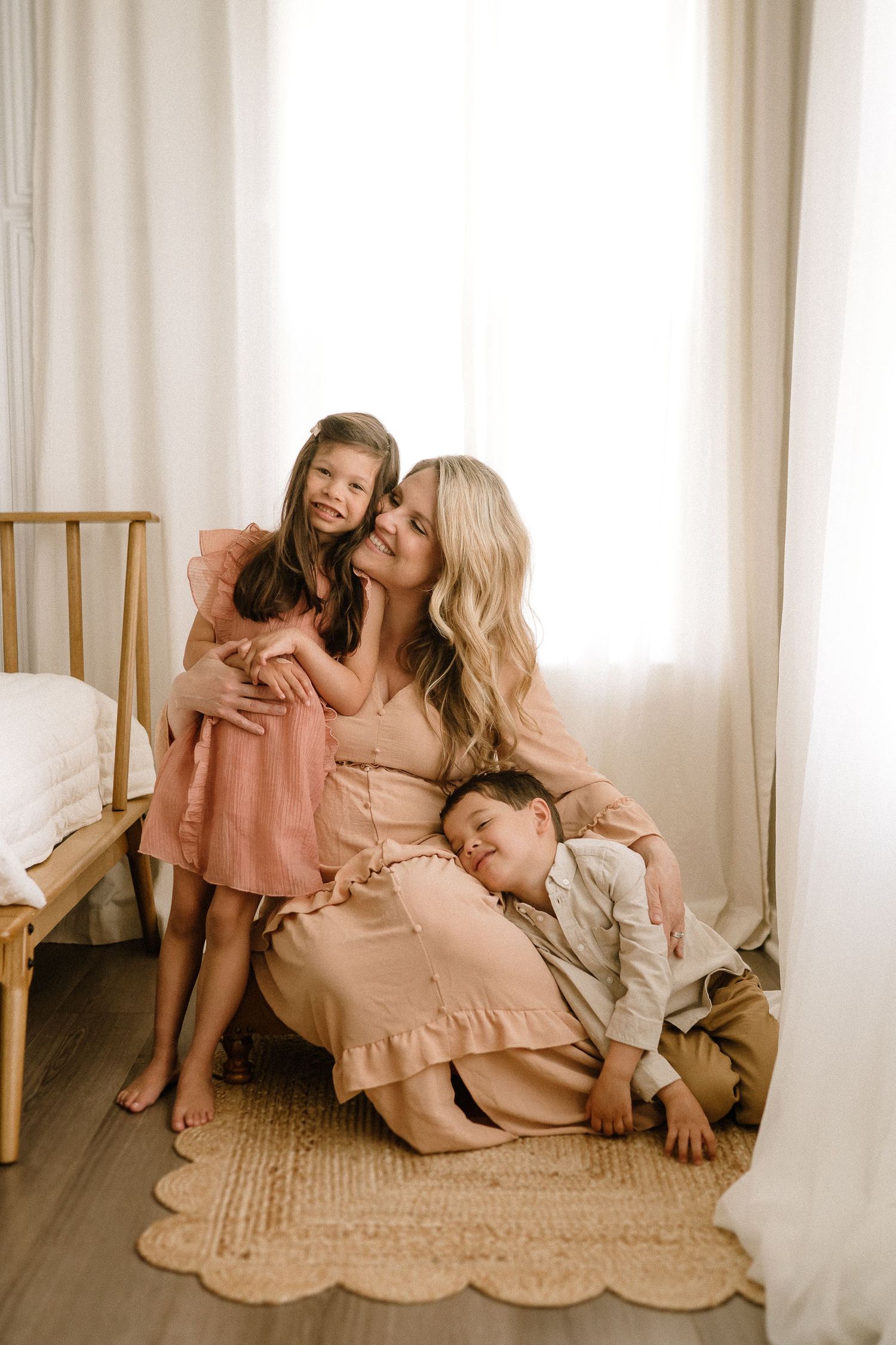 A heartwarming family portrait in soft peachy tones with a pregnant woman and children on a woven rug.