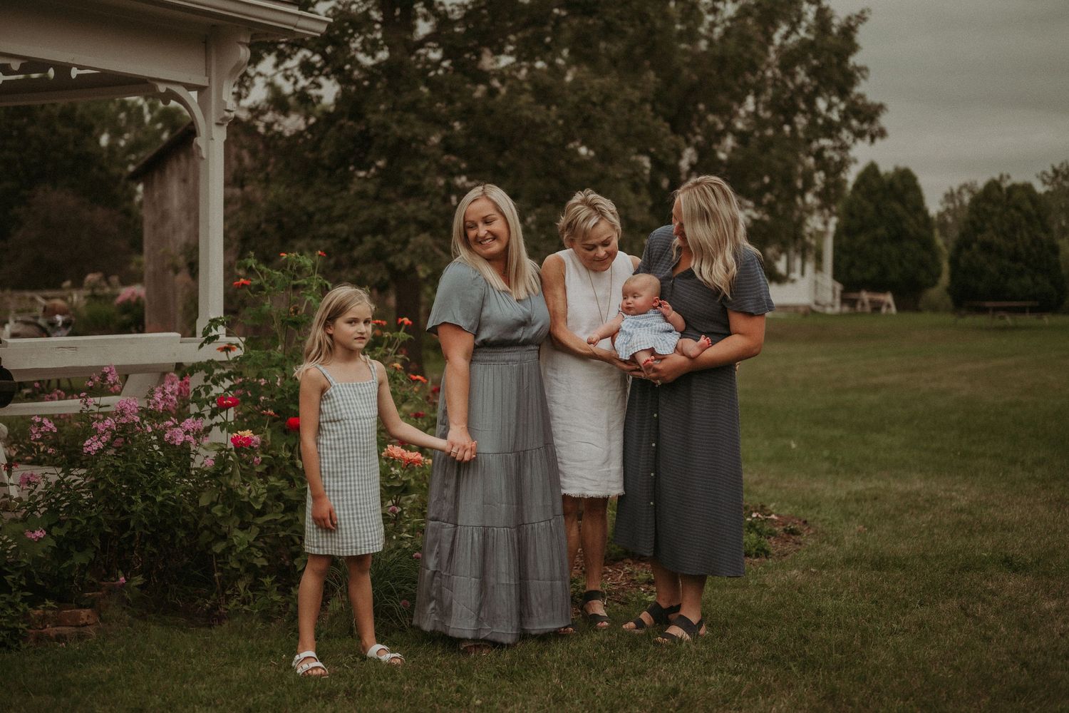 Four generations pose together in a garden setting with roses and gazebo.