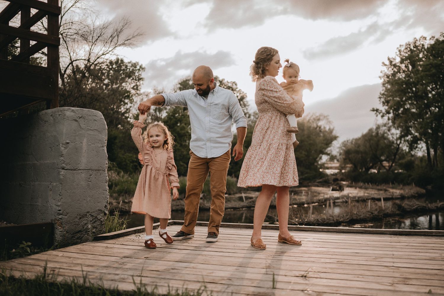 A family walks together on a wooden boardwalk during golden hour.