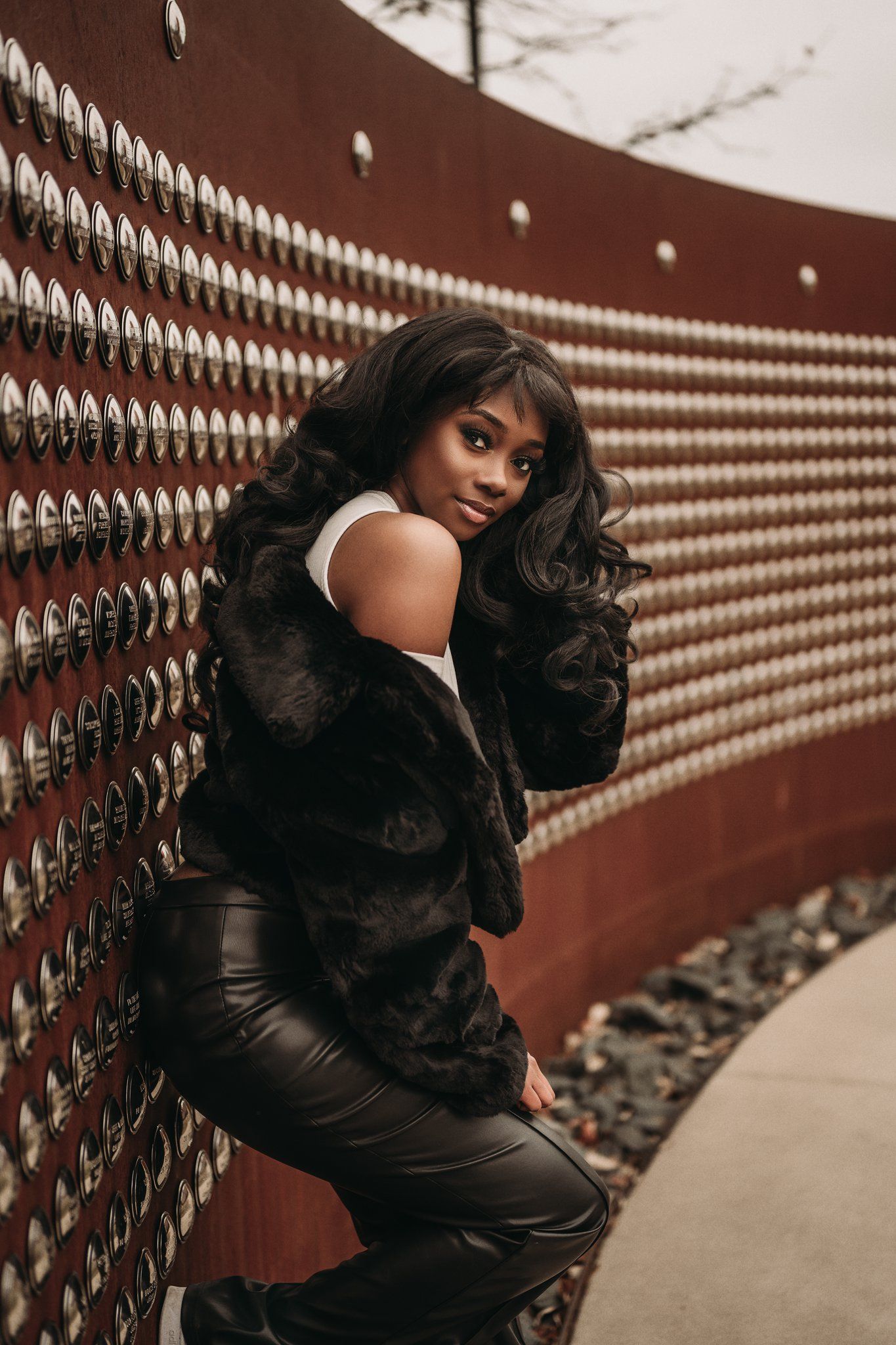 Fashion portrait against decorative red wall featuring fur coat and leather outfit.