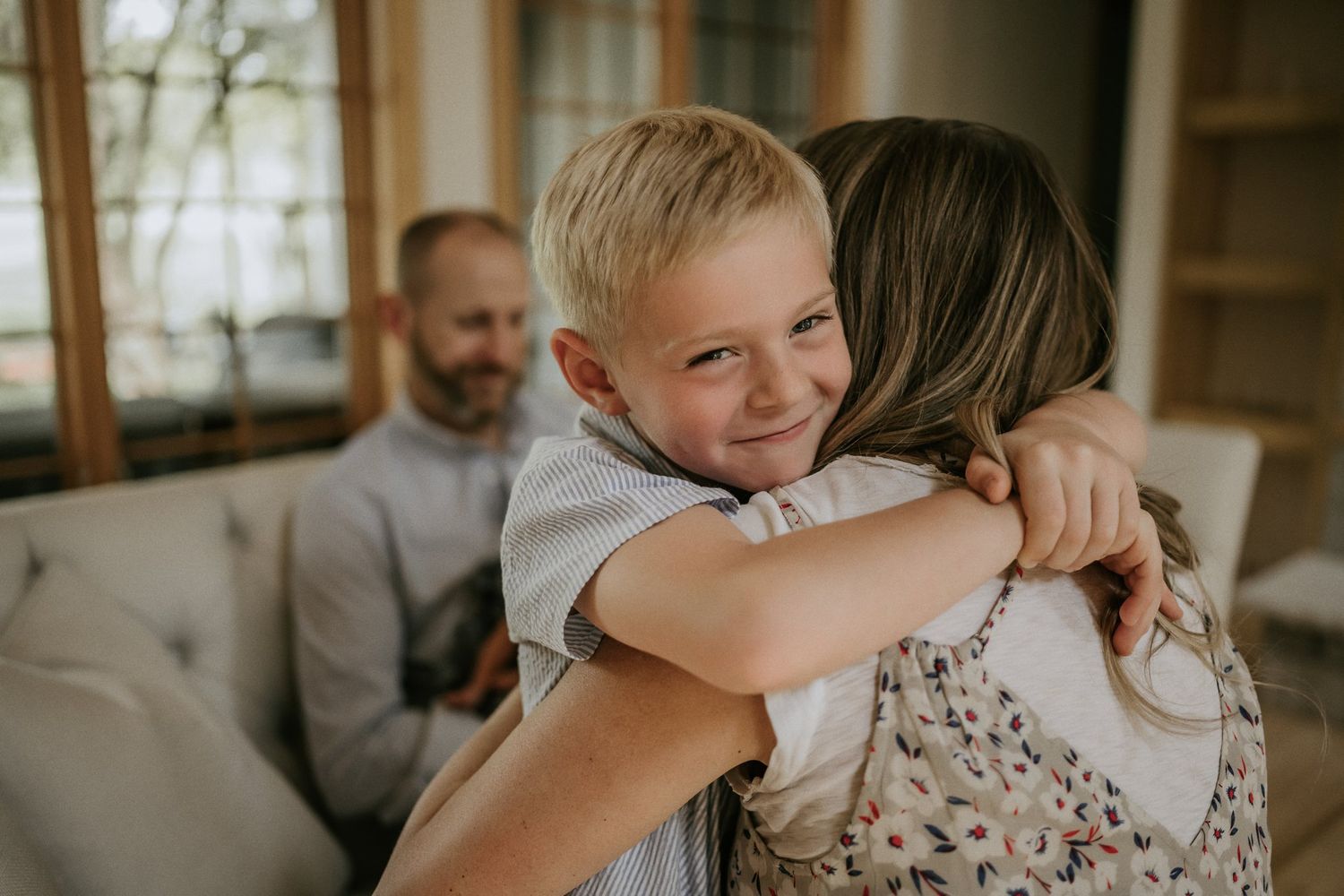 Warm family embrace captured in sunlit living room with natural decor.