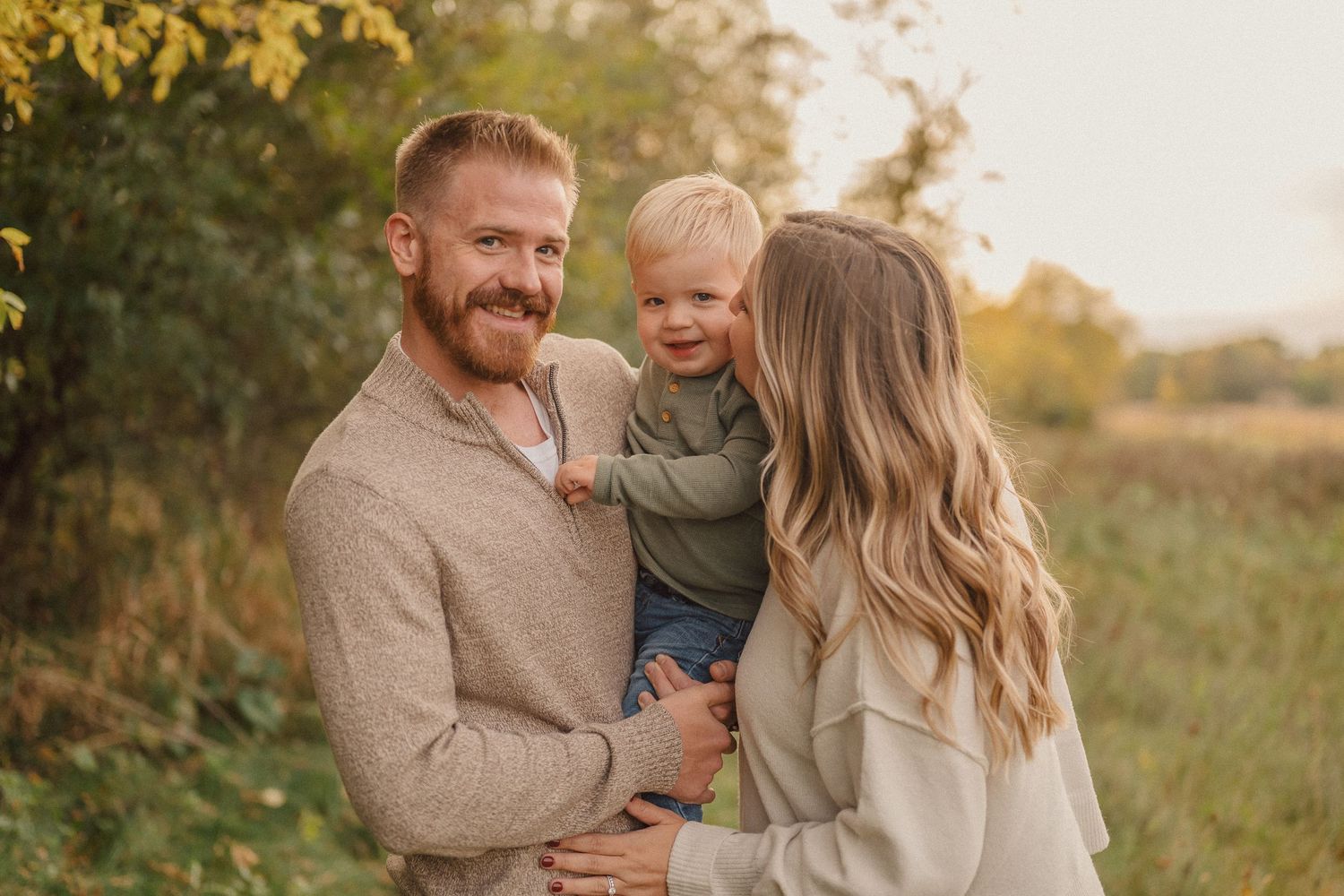 A family shares joyful moments together in a golden sunlit field during an outdoor photo session.