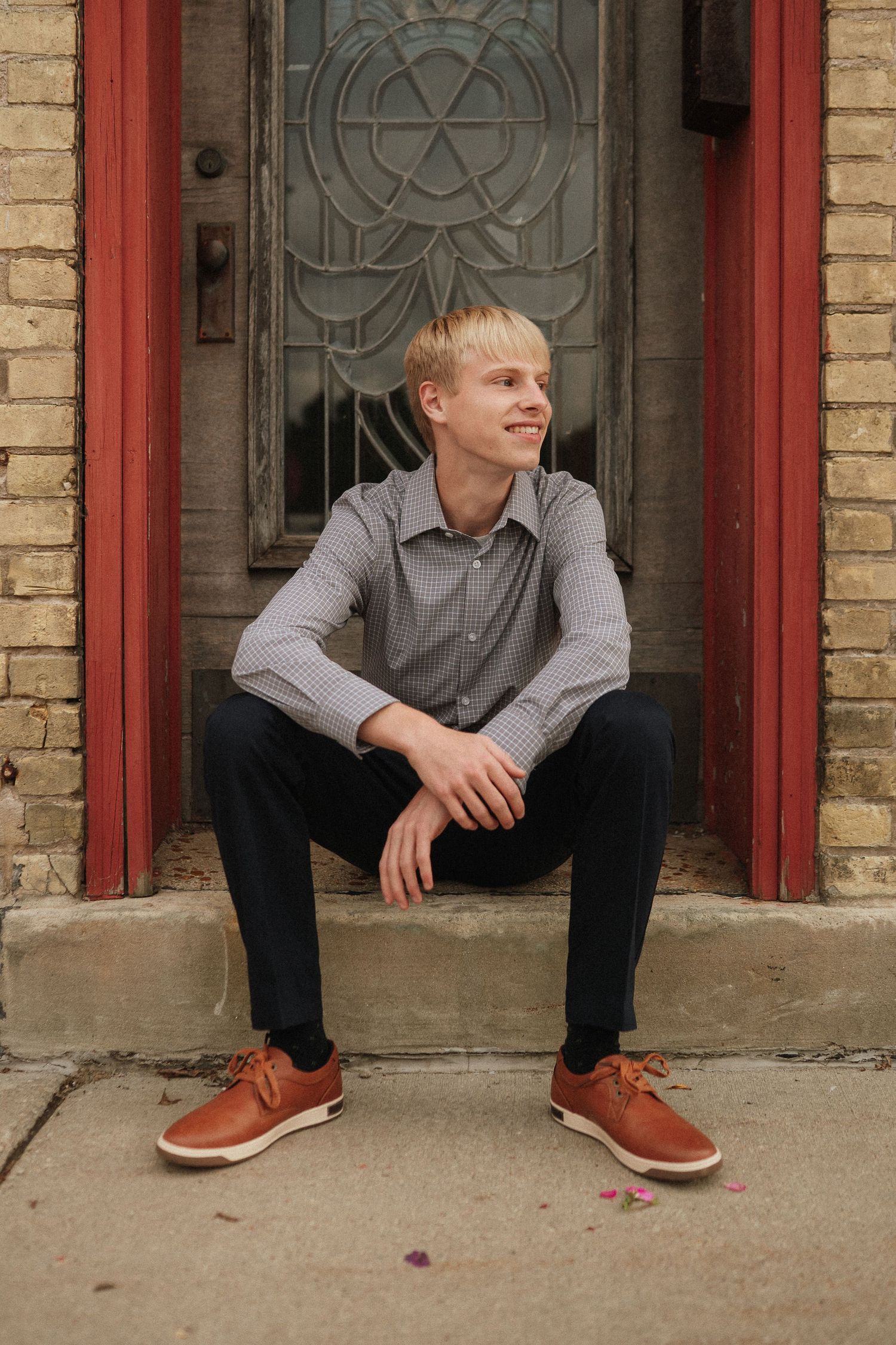 A series of casual poses sitting on stone steps against a brick wall with brown leather shoes.