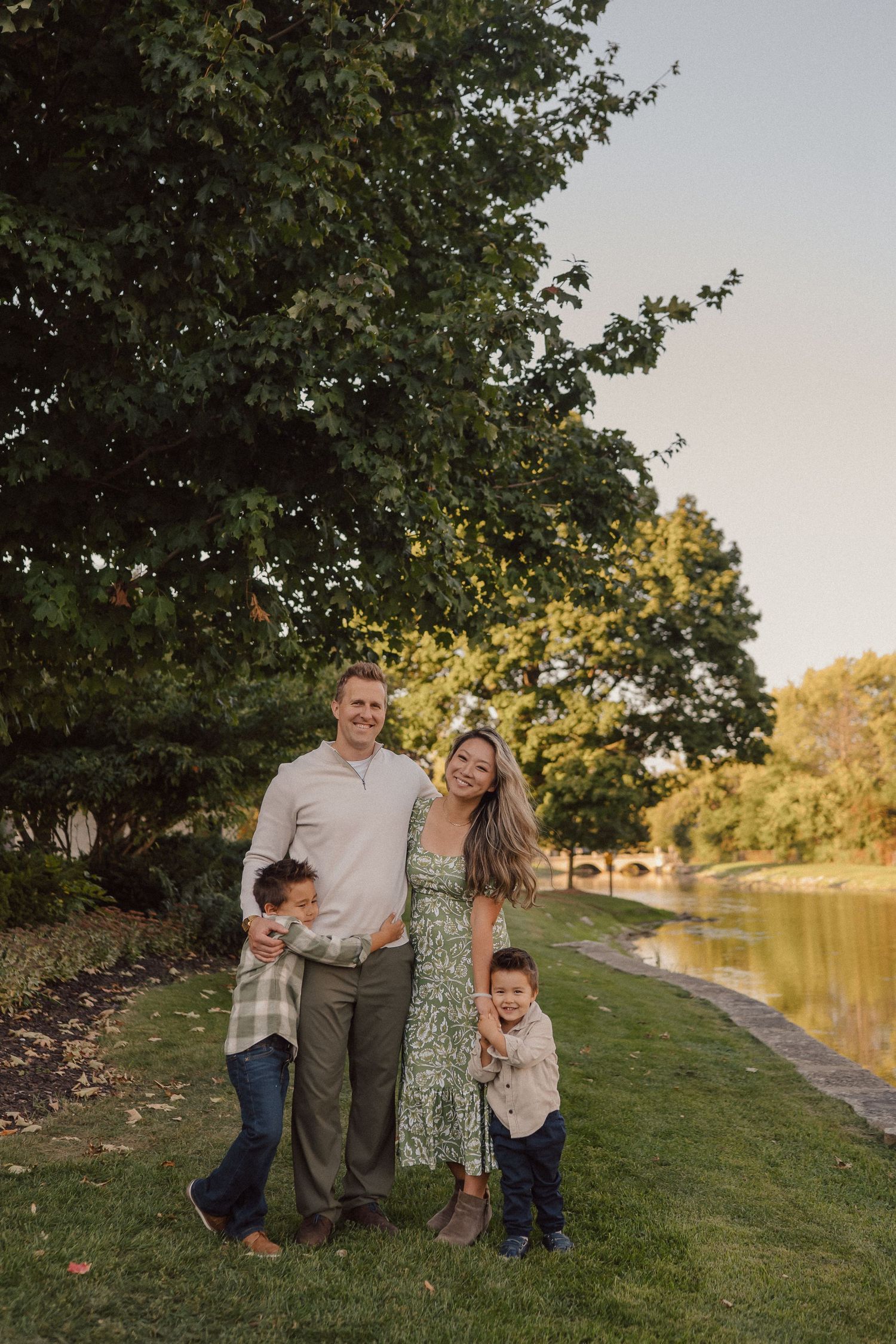 A family enjoys a warm autumn evening together by a peaceful river surrounded by golden foliage.