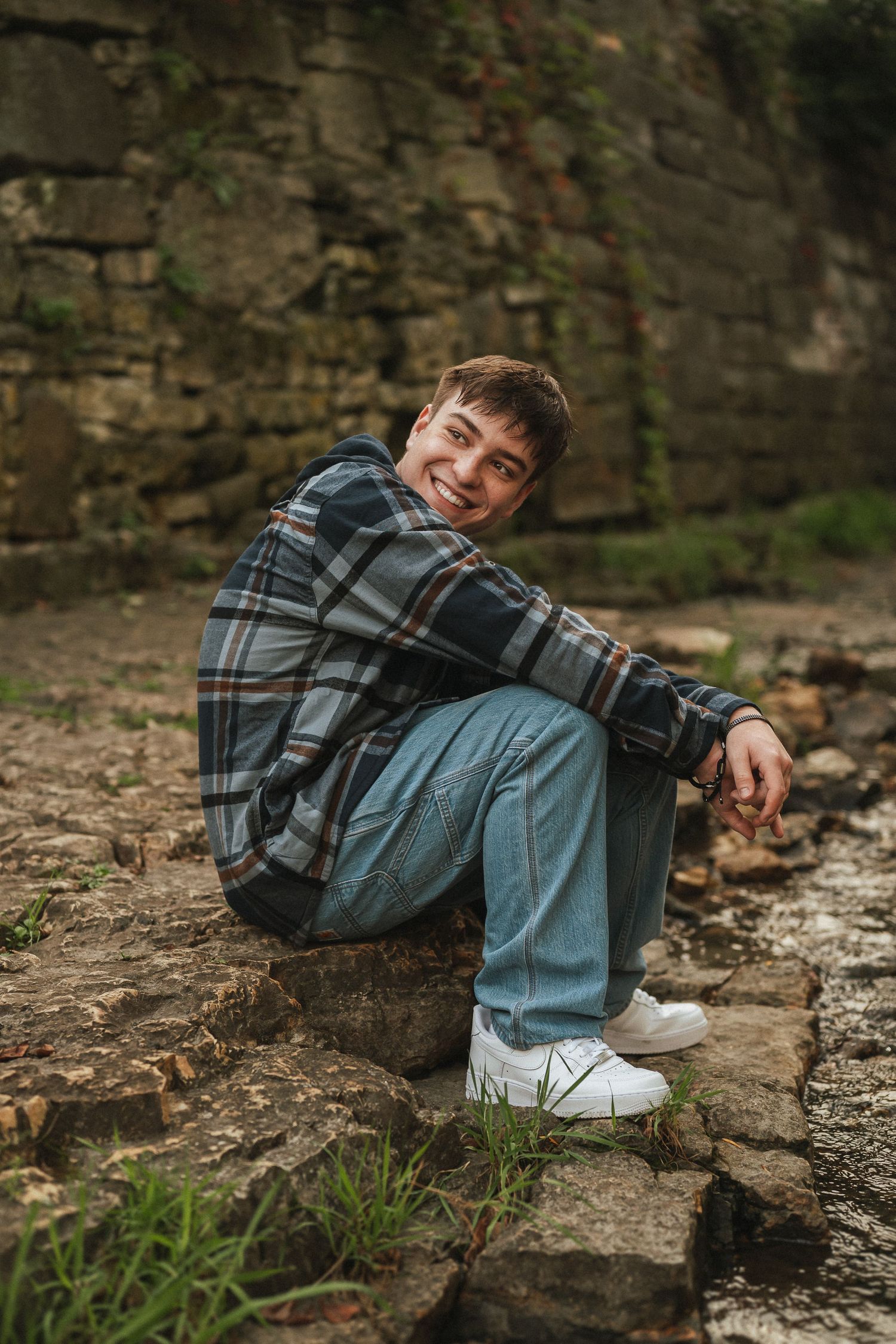 Person in plaid shirt and jeans lounging on stone steps in an outdoor setting.